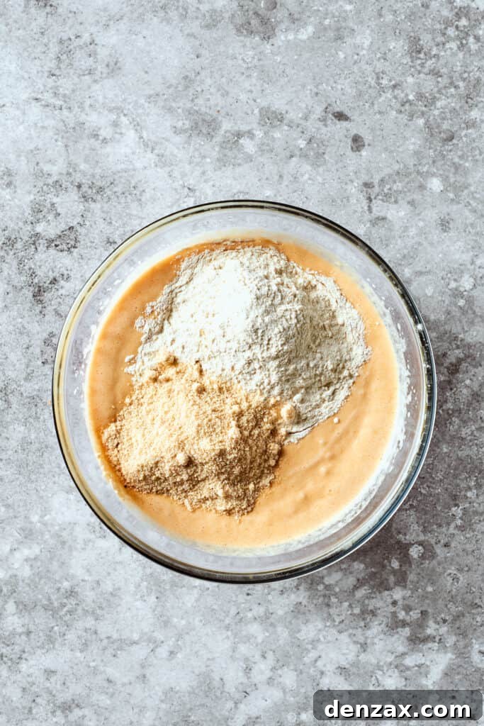 A generous cascade of all-purpose flour and almond flour is being sifted into the creamy wet mixture, ensuring a smooth, lump-free batter for the banana bread.