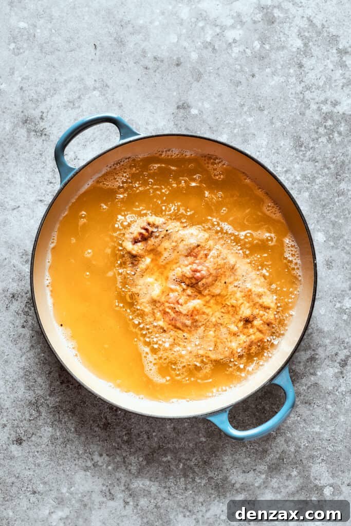 Breaded steak frying in hot oil in a skillet until golden brown.