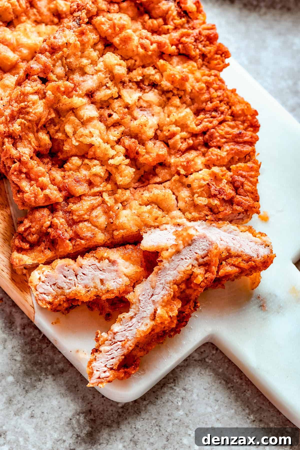A perfectly breaded, uncooked chicken fried steak resting on a wooden cutting board, ready for frying.