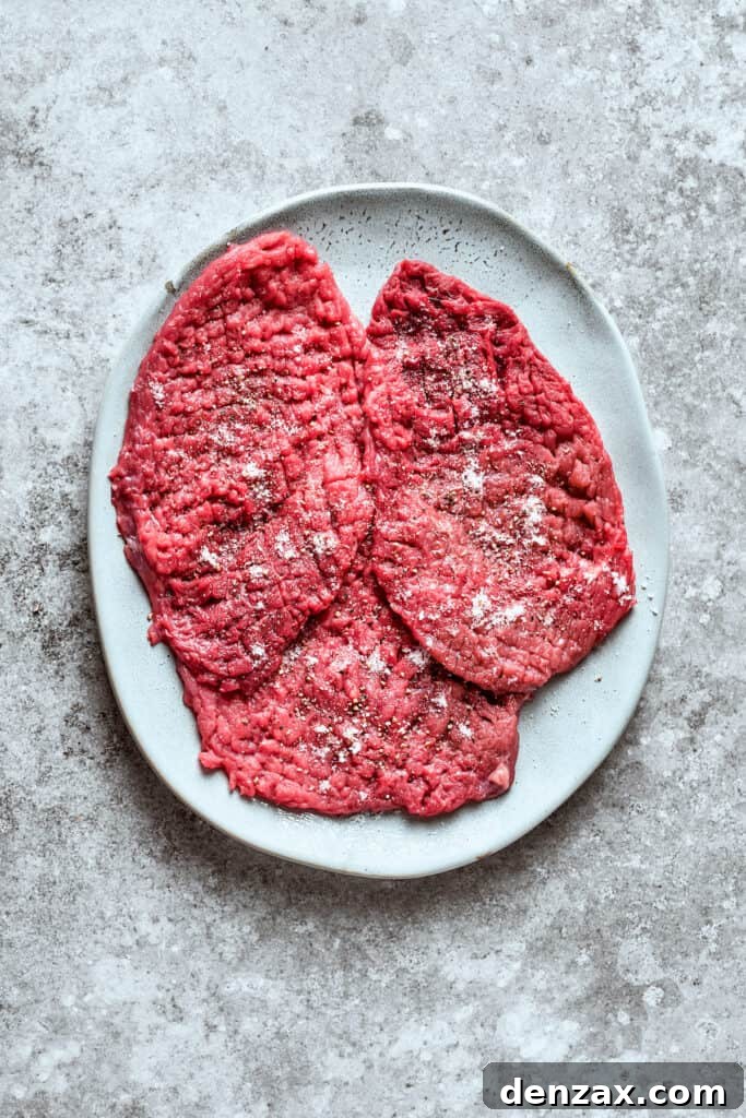 Three pieces of seasoned cube steak ready for dredging.