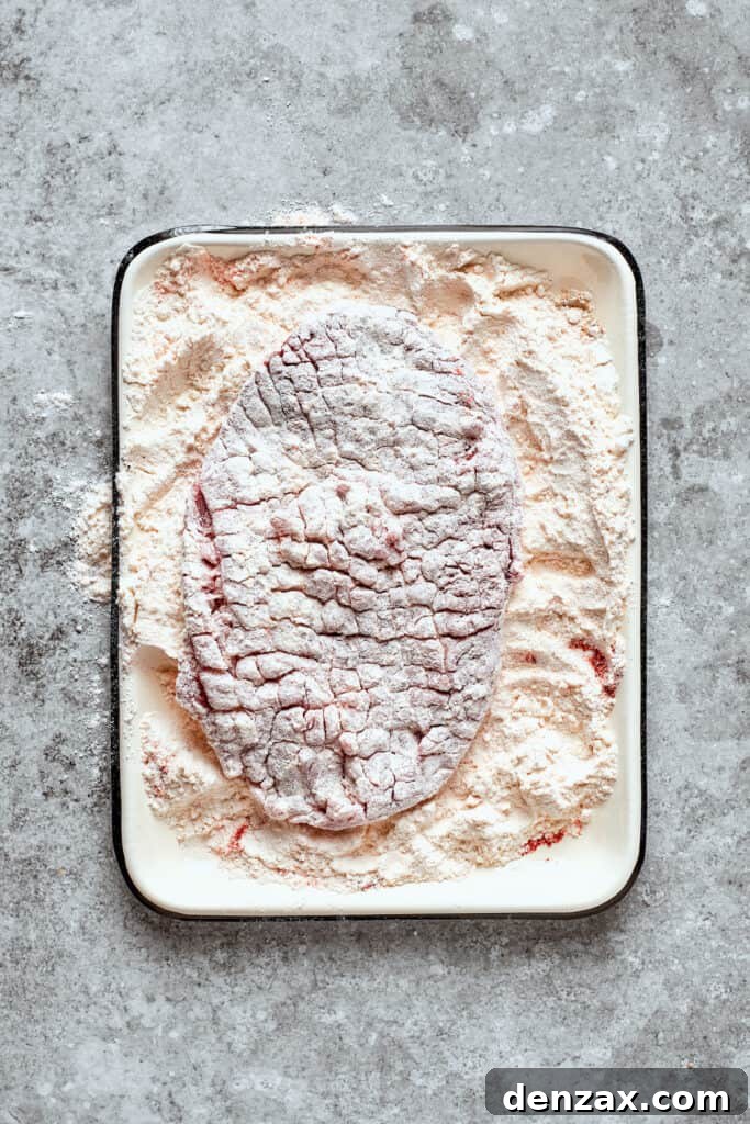 A cube steak being coated in the seasoned flour mixture.