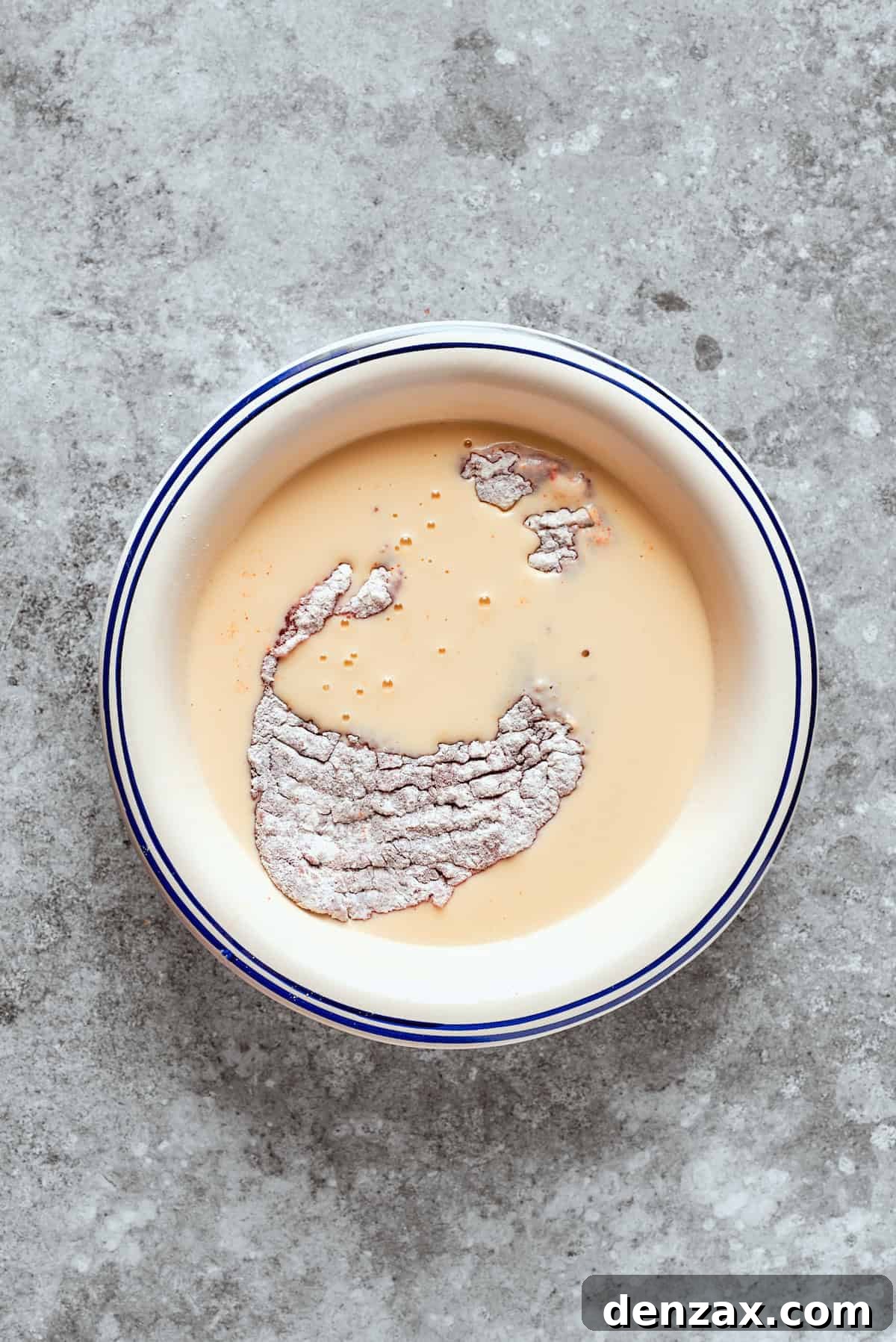 The flour-coated steak being dipped into the buttermilk and egg mixture.