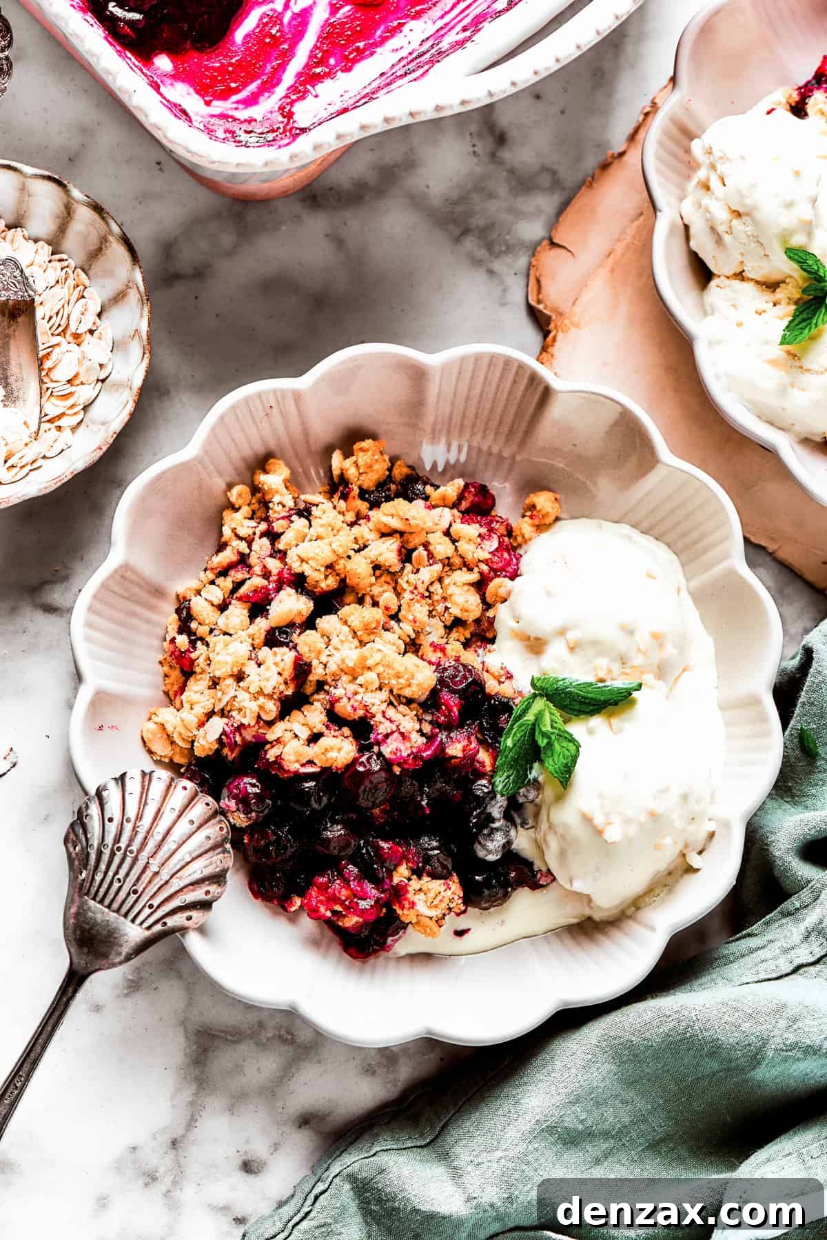 Blueberry crisp served in a bowl with two scoops of vanilla ice cream and a garnish of mint.