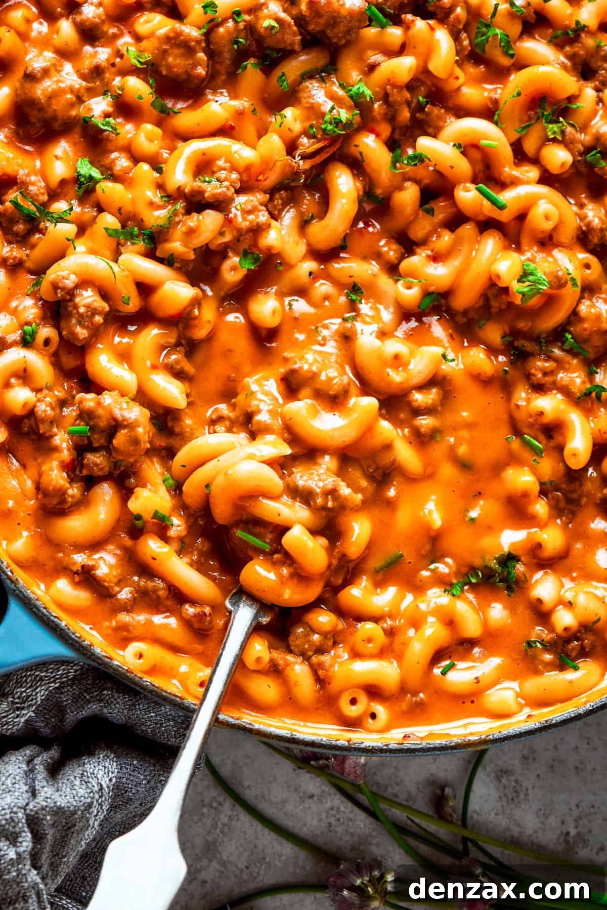 A spoon stirring through homemade hamburger helper in a skillet, showcasing the creamy sauce, ground beef, and pasta.