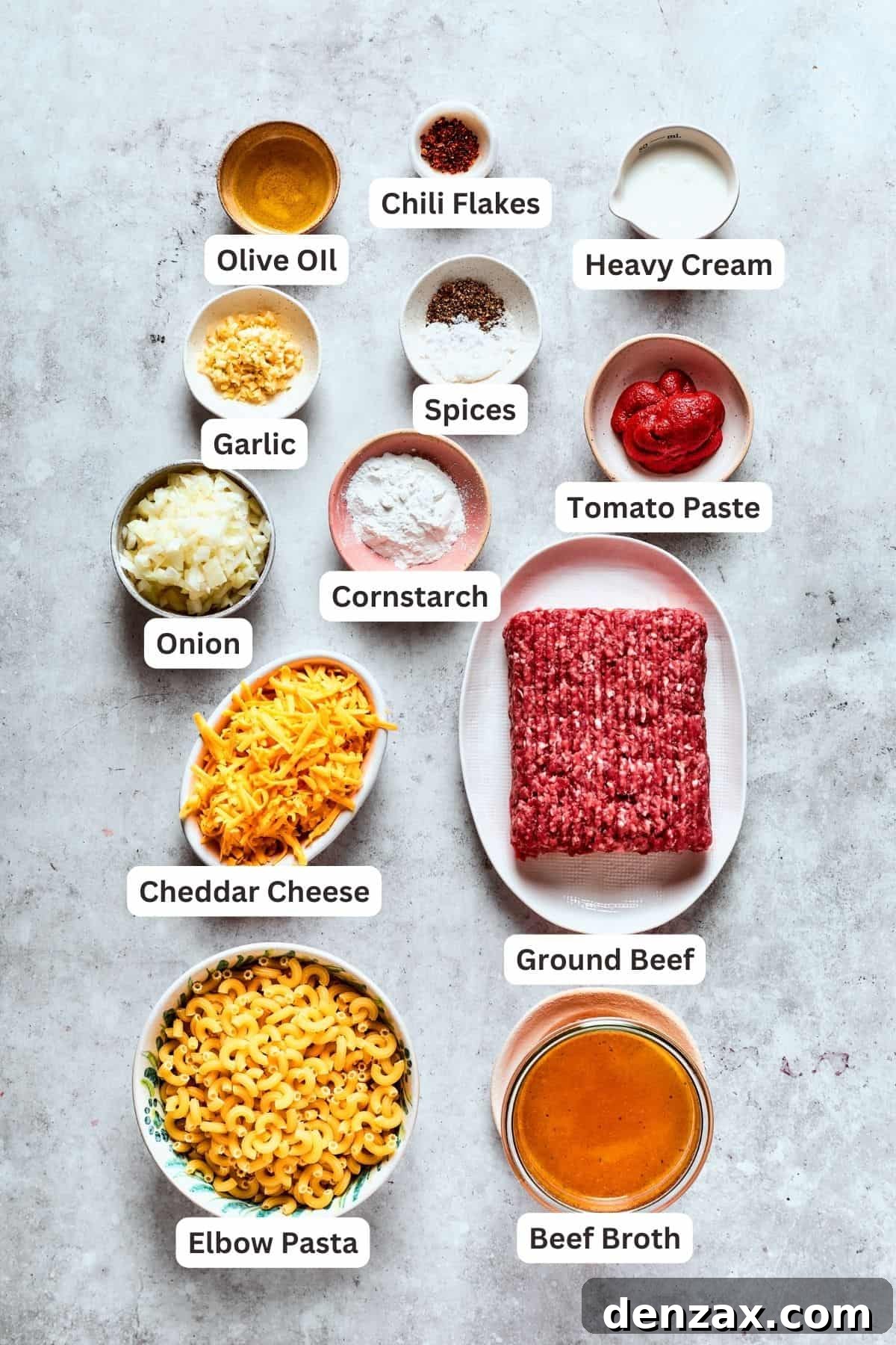 Ingredients for homemade hamburger helper laid out: ground beef, macaroni pasta, cheddar cheese, onion, garlic, tomato paste, cornstarch, heavy cream, olive oil, and various seasonings.
