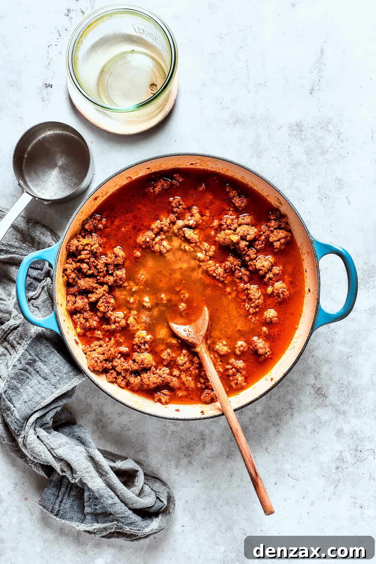 Ground beef cooking in a pan with broth and tomato puree, forming a rich sauce.