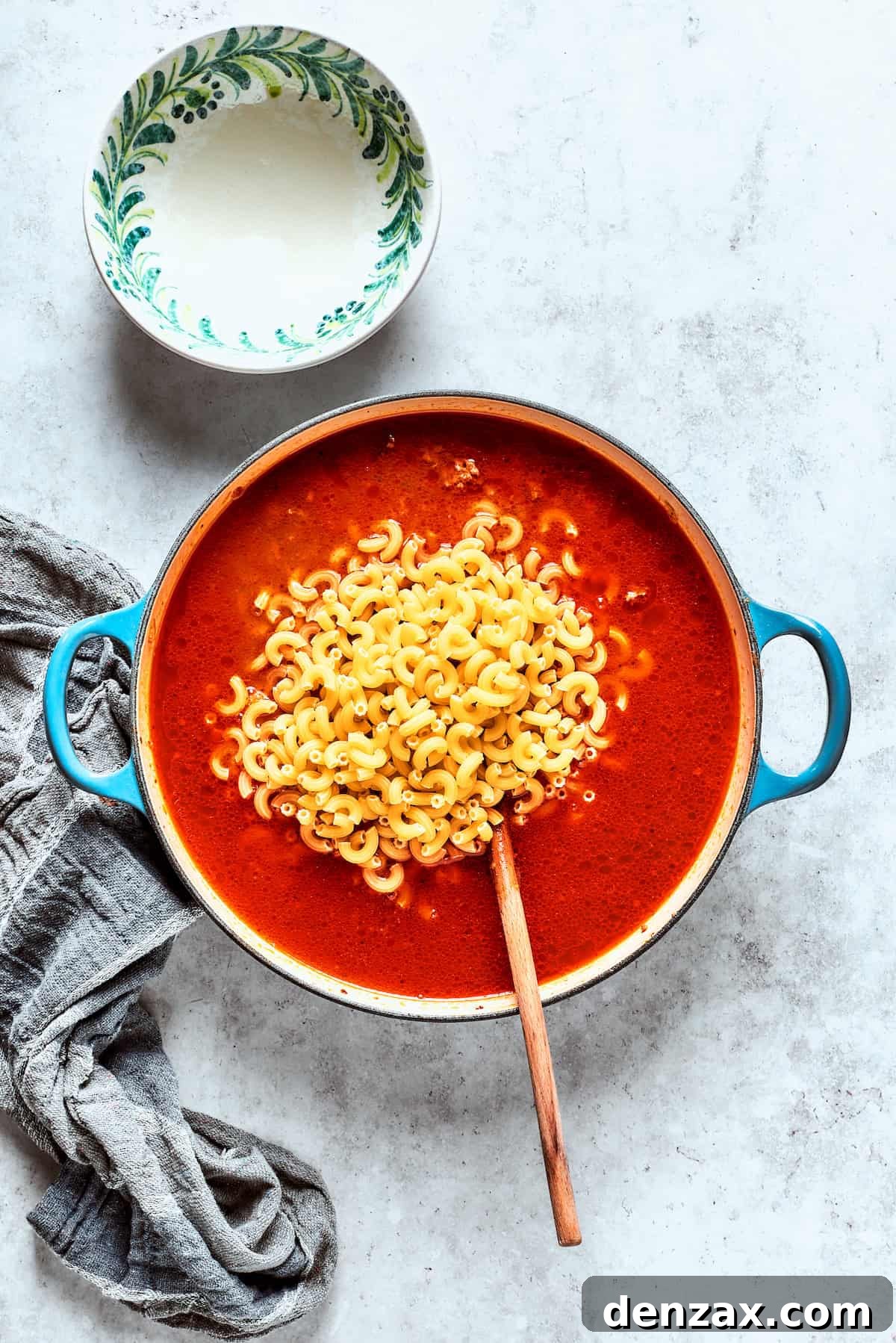Elbow pasta being added to the pan with the beef and broth mixture, ready to cook.