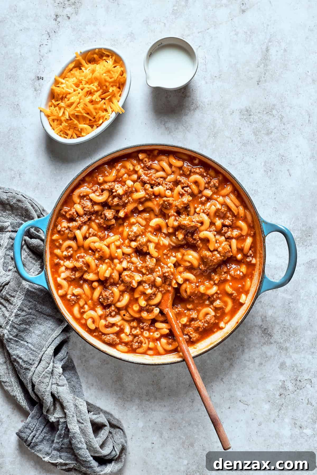 A spoon stirring together the pasta and beef mixture as it cooks, ensuring even distribution.