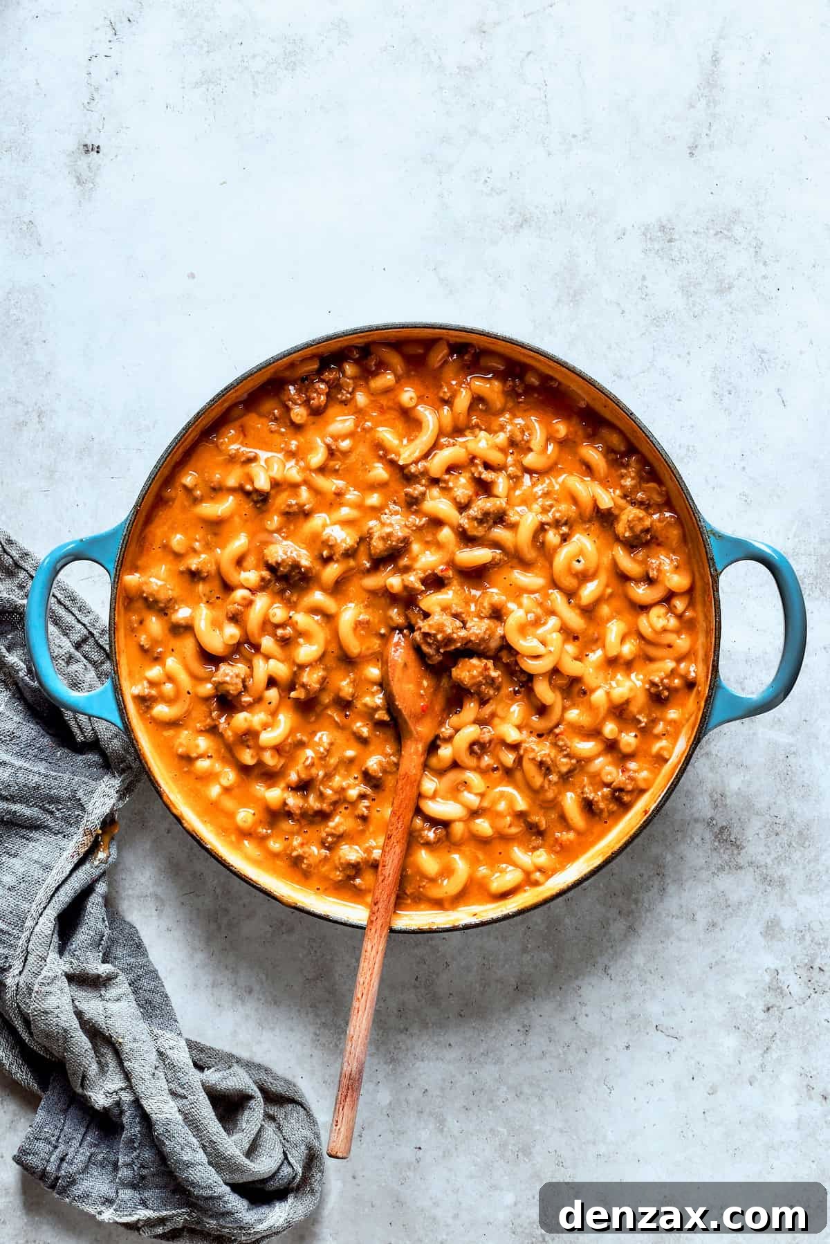 Shredded cheddar cheese and heavy cream being stirred into the cooked hamburger helper, creating a creamy, cheesy sauce.