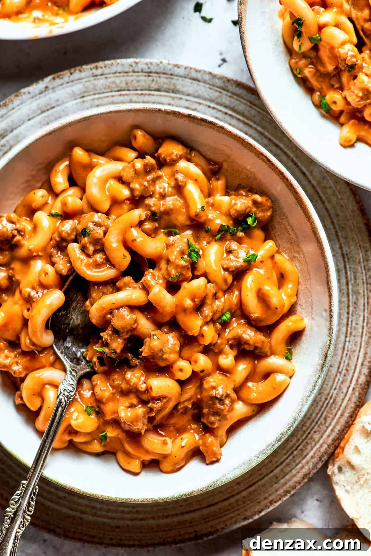 A bowl of creamy macaroni and ground beef sauce, garnished with fresh herbs, ready to be enjoyed.
