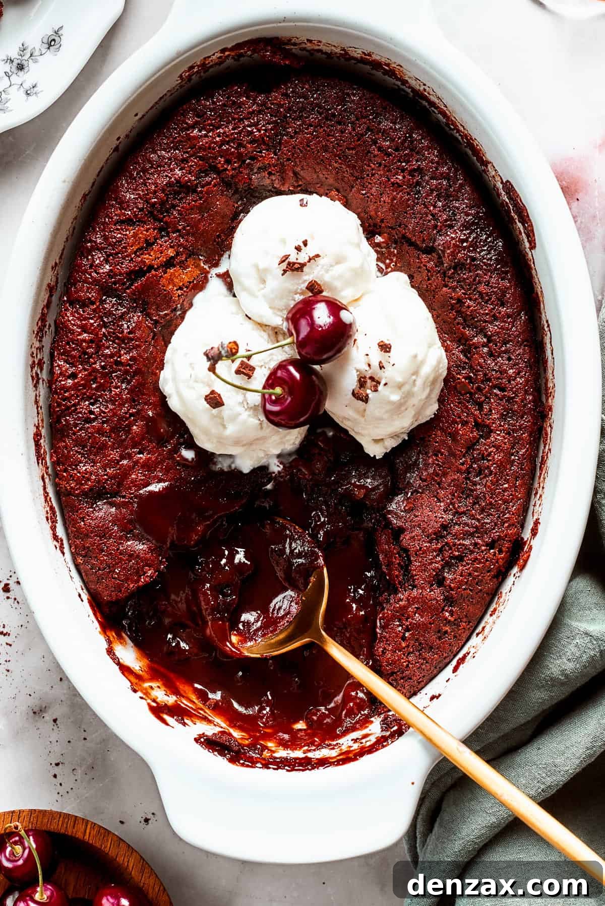An oval casserole dish showcasing a warm chocolate pudding cake generously topped with melting vanilla ice cream and a spoon ready to dive in.
