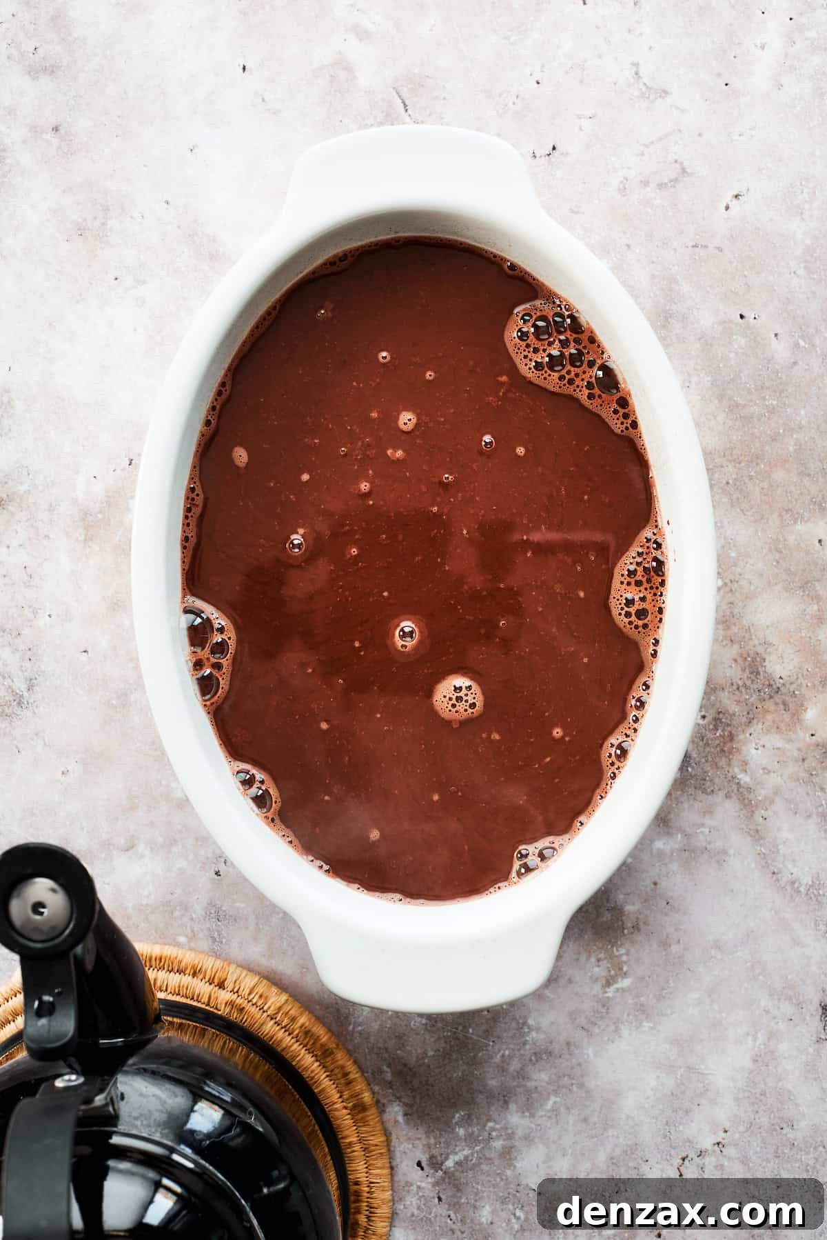 Boiling water is carefully and slowly poured over the fudge topping and cake batter in the pan, a crucial step for the self-saucing magic.