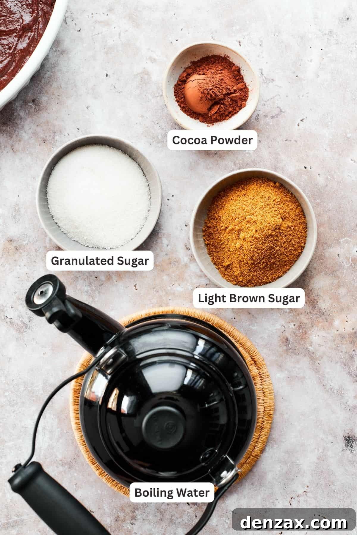 Labeled ingredients for the chocolate pudding cake topping, including boiling water, brown sugar, granulated sugar, and cocoa powder, arranged on a surface.