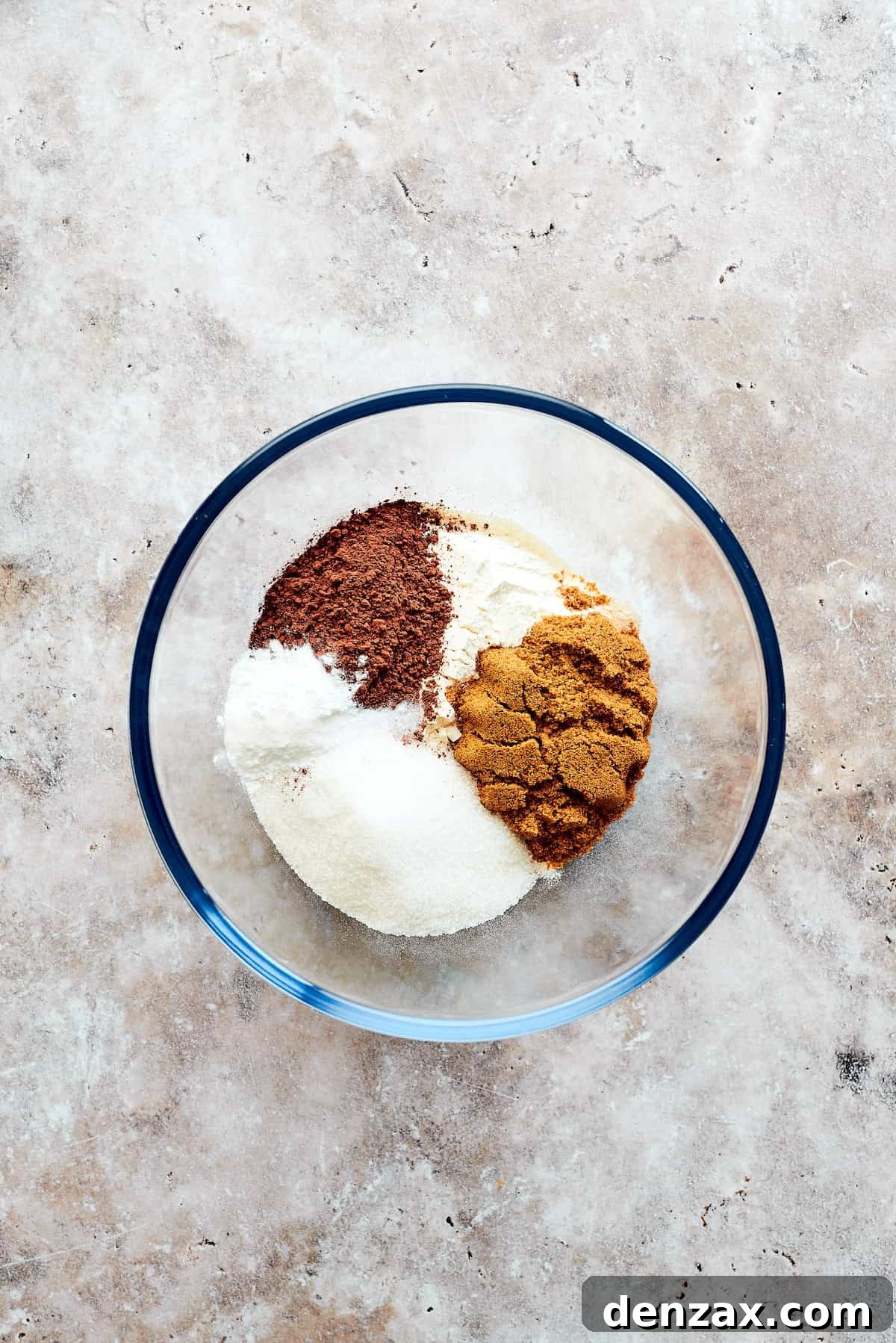 Dry ingredients for chocolate pudding cake, including flour, cocoa powder, and sugars, being added to a large mixing bowl.