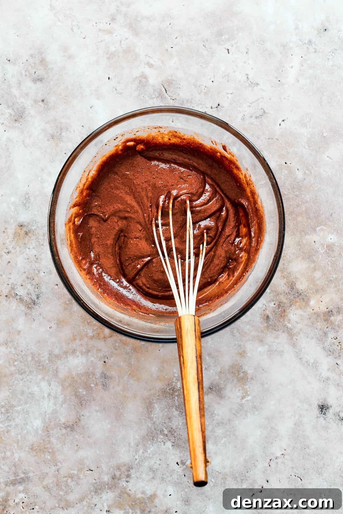 A whisk smoothly combines the wet and dry ingredients, forming the rich chocolate cake batter in a mixing bowl.