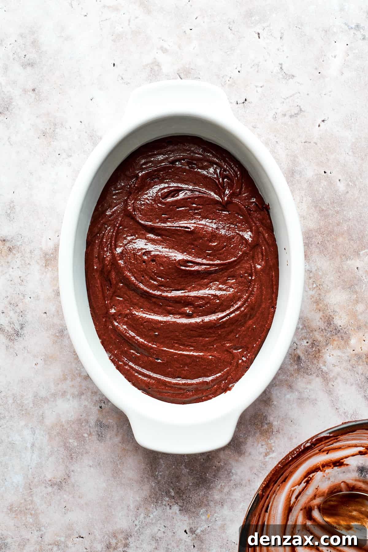 The prepared chocolate pudding cake batter is poured evenly into an oval baking dish, ready for the next steps.