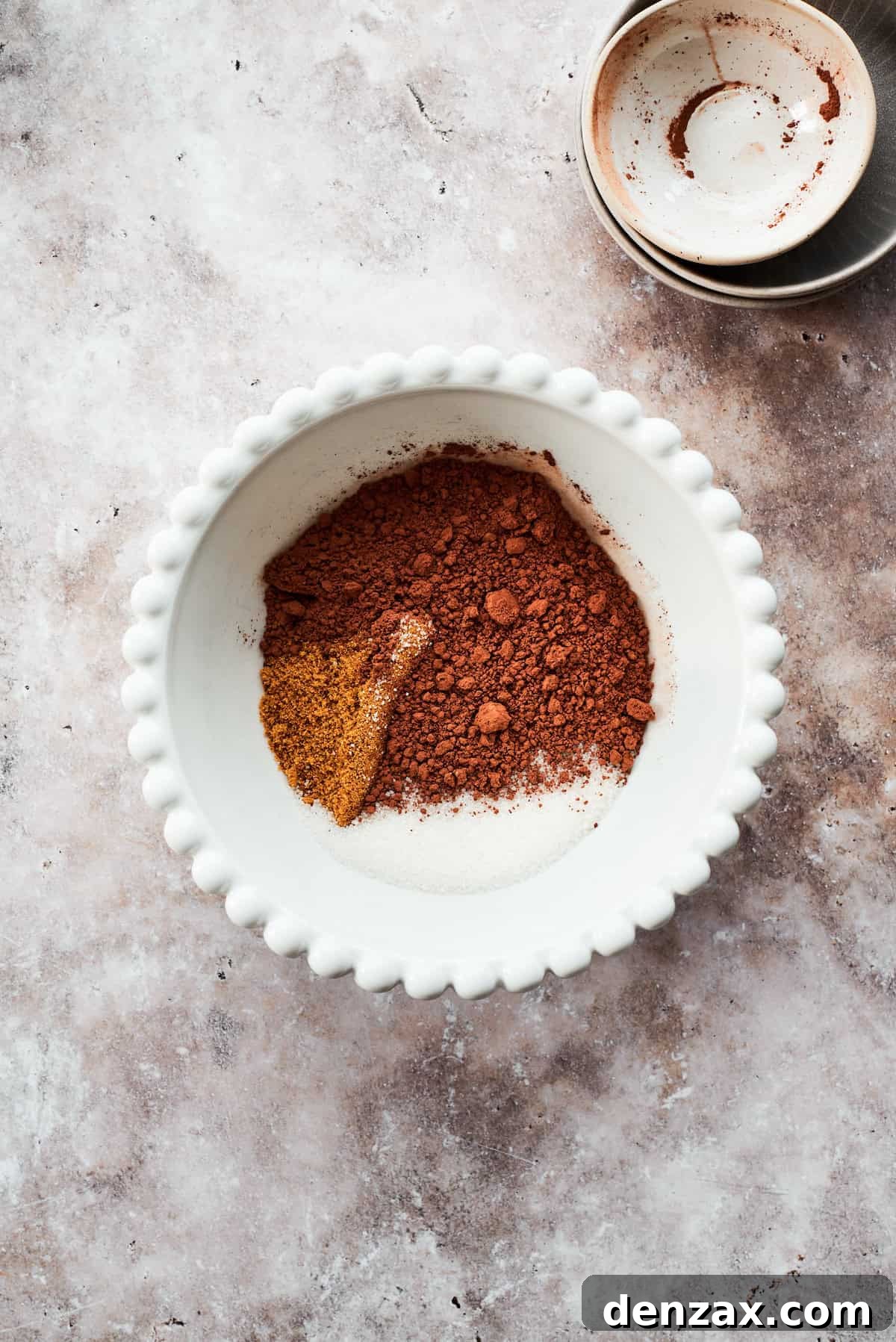 The dry ingredients for the fudge topping – granulated sugar, brown sugar, and cocoa powder – are carefully added to a small mixing bowl.