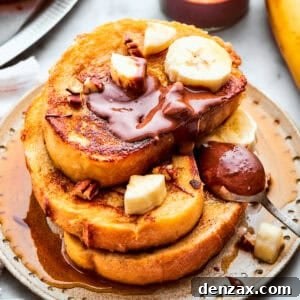 Three golden-brown slices of Banana French Toast are stacked on a white plate, beautifully garnished with fresh banana slices and a swirl of chocolate hazelnut spread. The toast appears fluffy and inviting.
