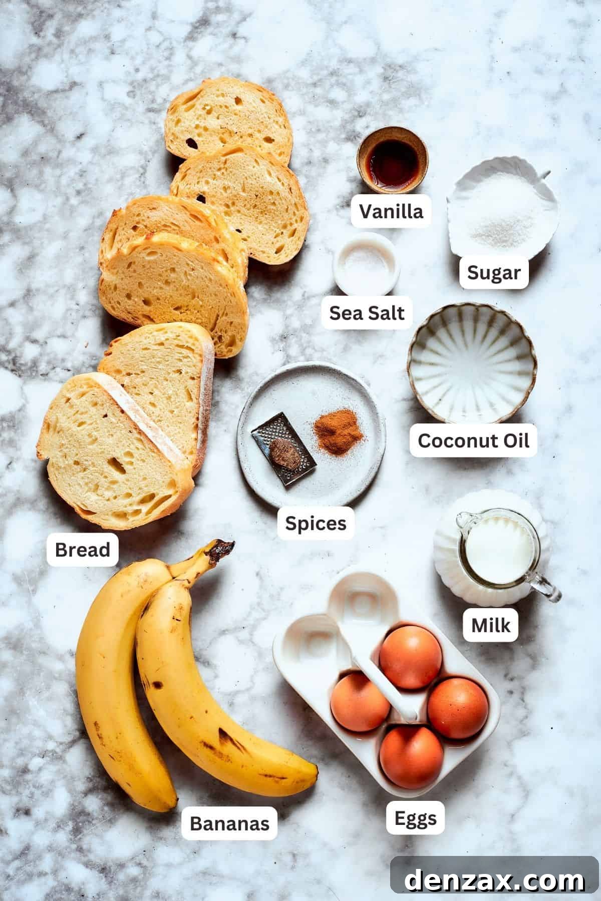 All the essential ingredients for crafting perfect Banana French Toast are neatly laid out: ripe bananas, slices of thick bread, a bowl of eggs, a jug of milk, and small bowls containing cinnamon, nutmeg, salt, sugar, and vanilla extract. Coconut oil is also visible.