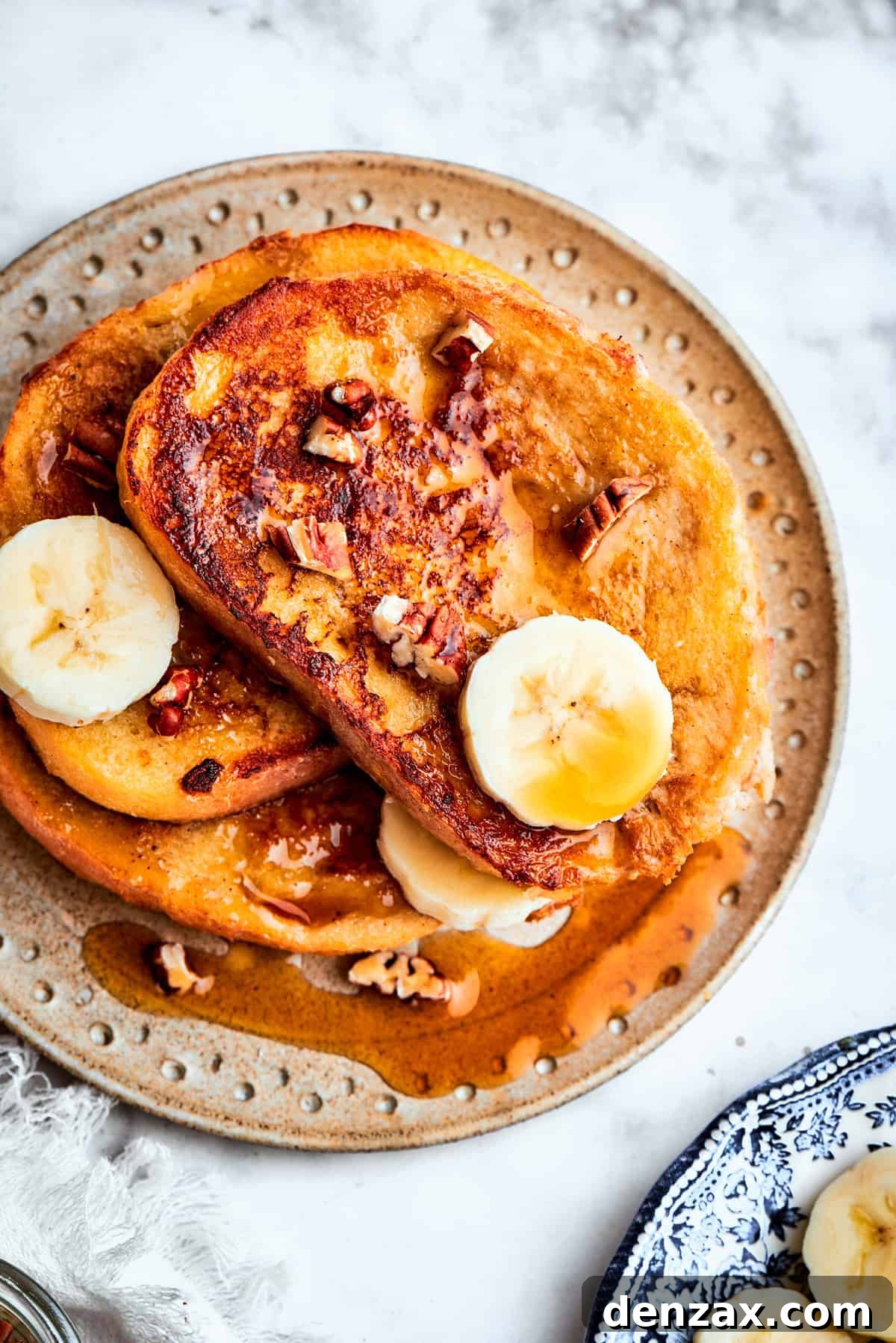 A single slice of perfectly cooked Banana French Toast sits on a white plate, adorned with neatly fanned banana slices on top and a light dusting of powdered sugar. The toast looks fluffy and inviting.