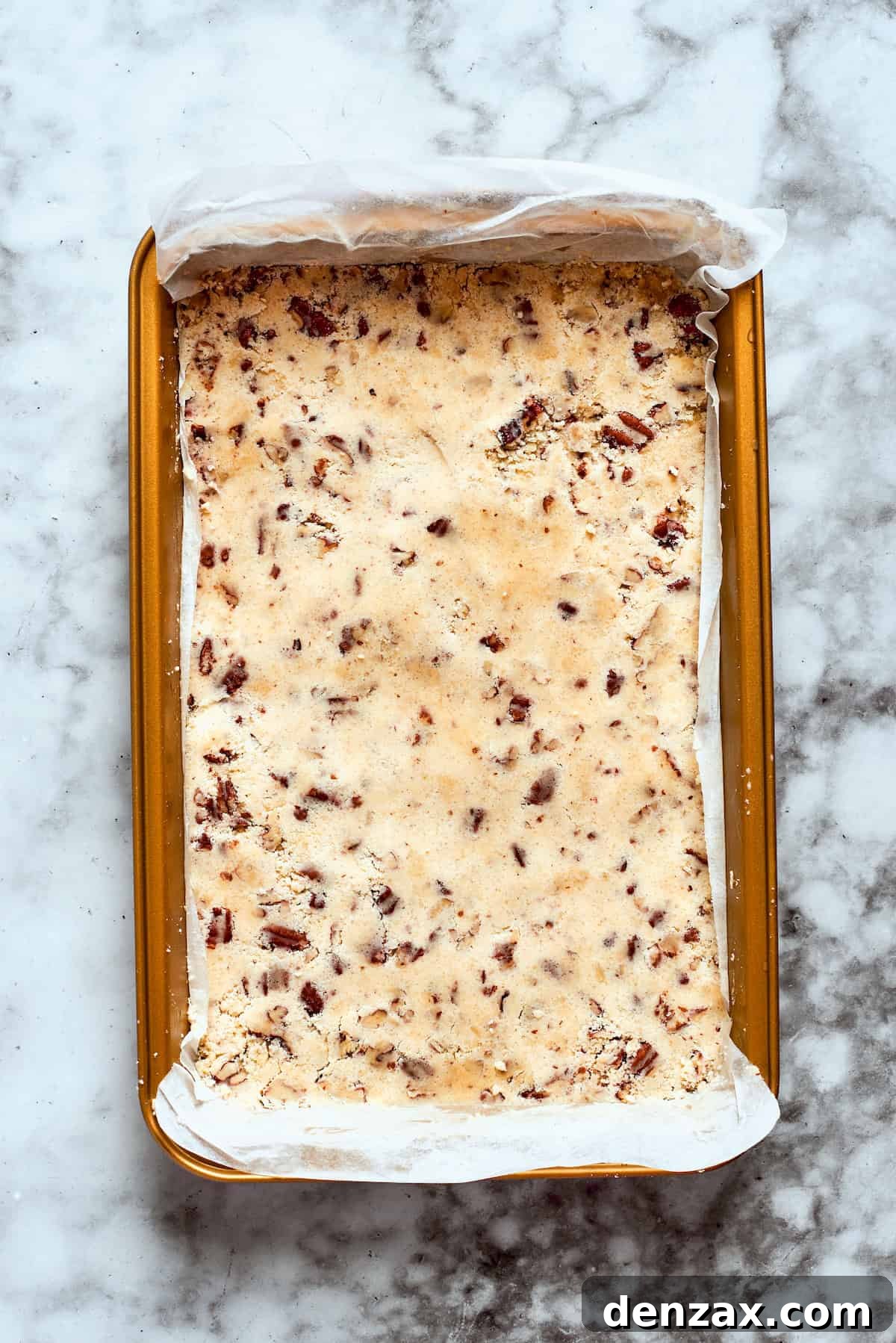 The prepared pecan crust mixture is evenly pressed into the bottom of a 9x13 inch baking dish, ready for baking.