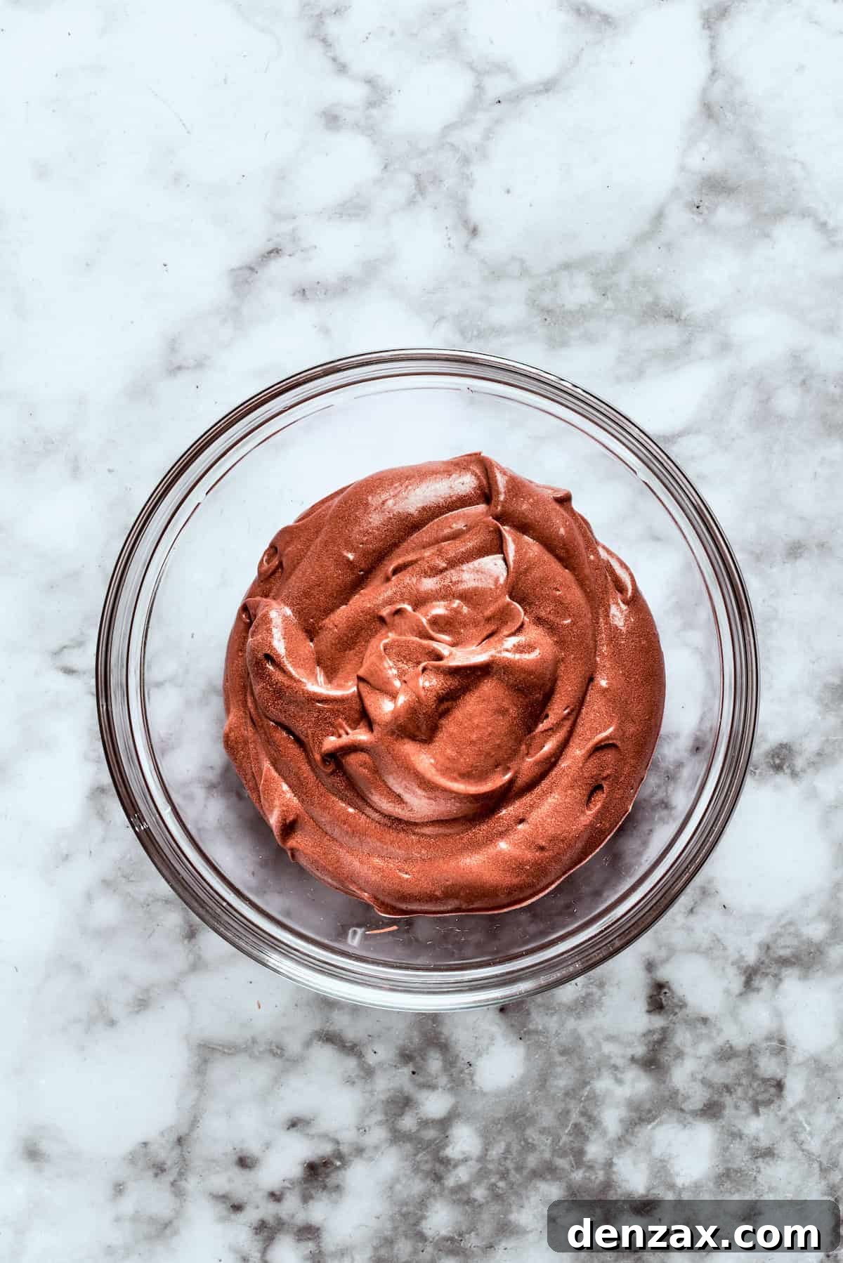 Instant chocolate pudding mix and milk are whisked together in a bowl until they form a thick, smooth chocolate pudding, ready for layering.