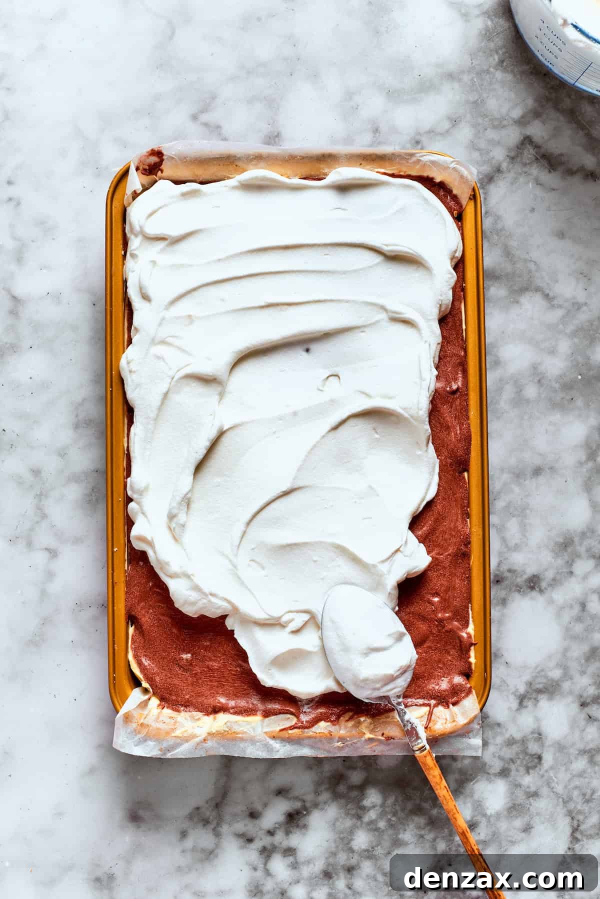 A generous layer of Cool Whip is being evenly spread over the top of the chocolate pudding layer, preparing the dessert for its final chilling stage.