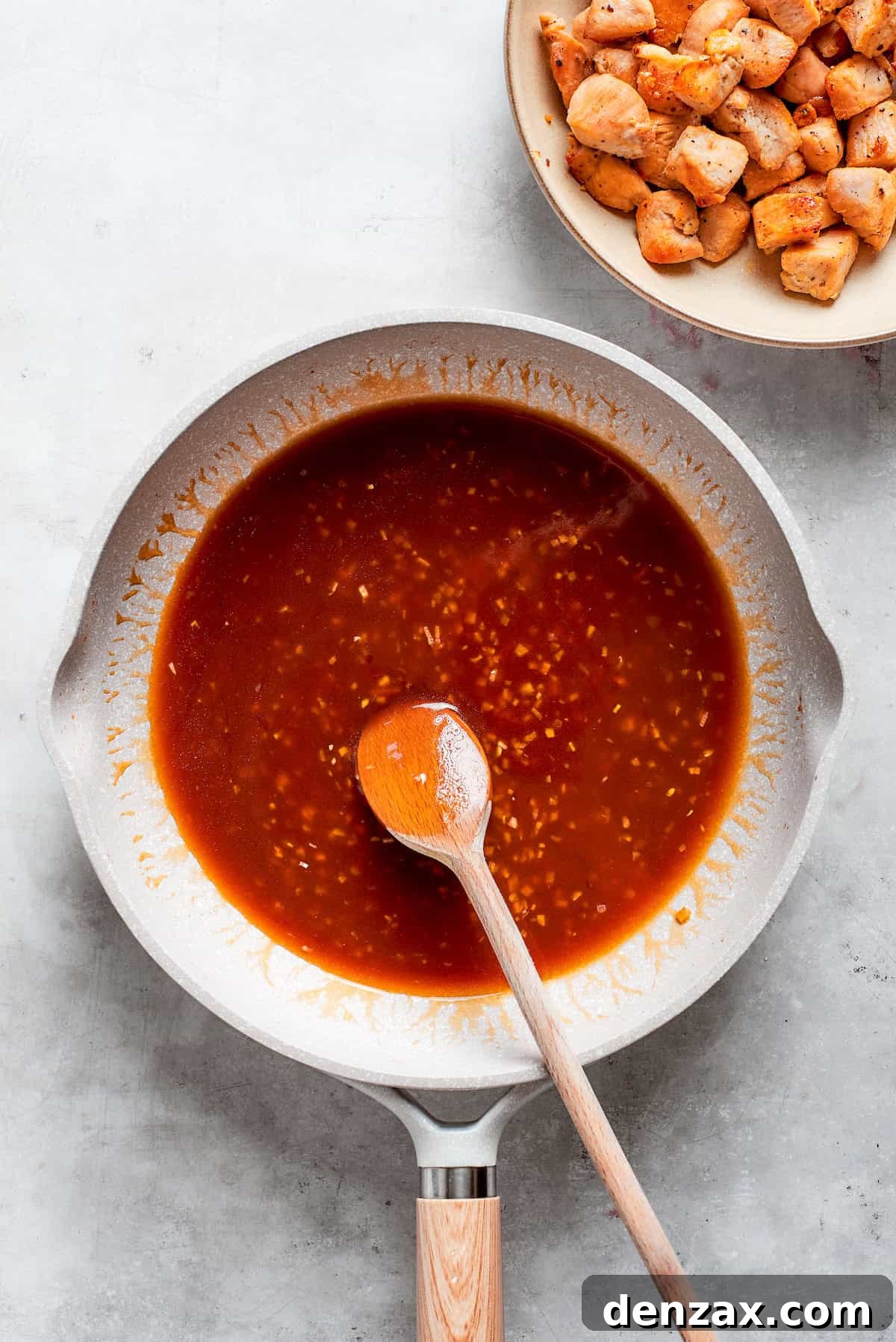 This Teriyaki Chicken Recipe folds tender bites of chicken into a thick, homemade teriyaki sauce for a savory and flavorful dish. A spoon combines the teriyaki sauce in a pan.
