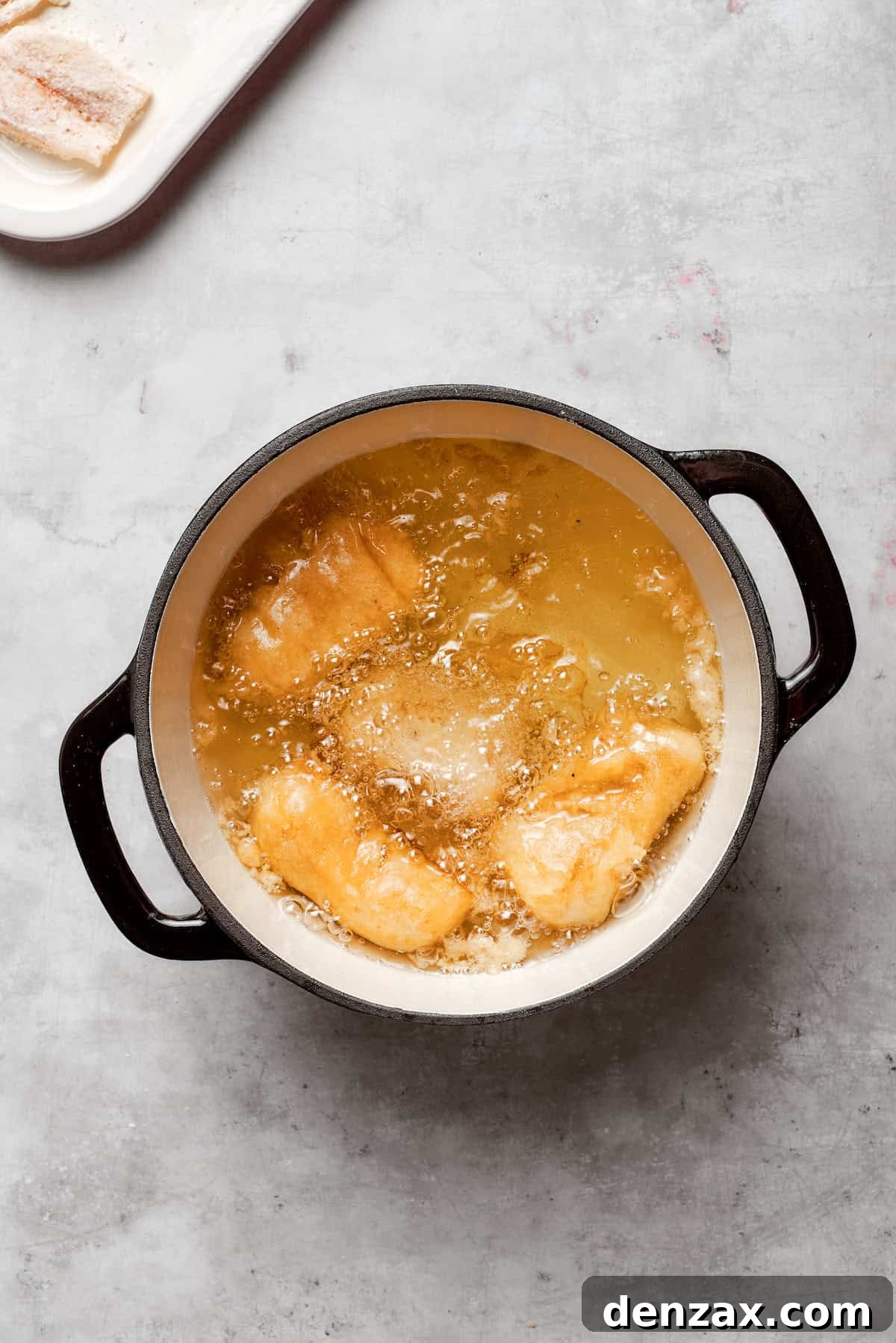 Pieces of beer-battered fish are frying in a pot of hot oil, bubbling and turning golden brown.
