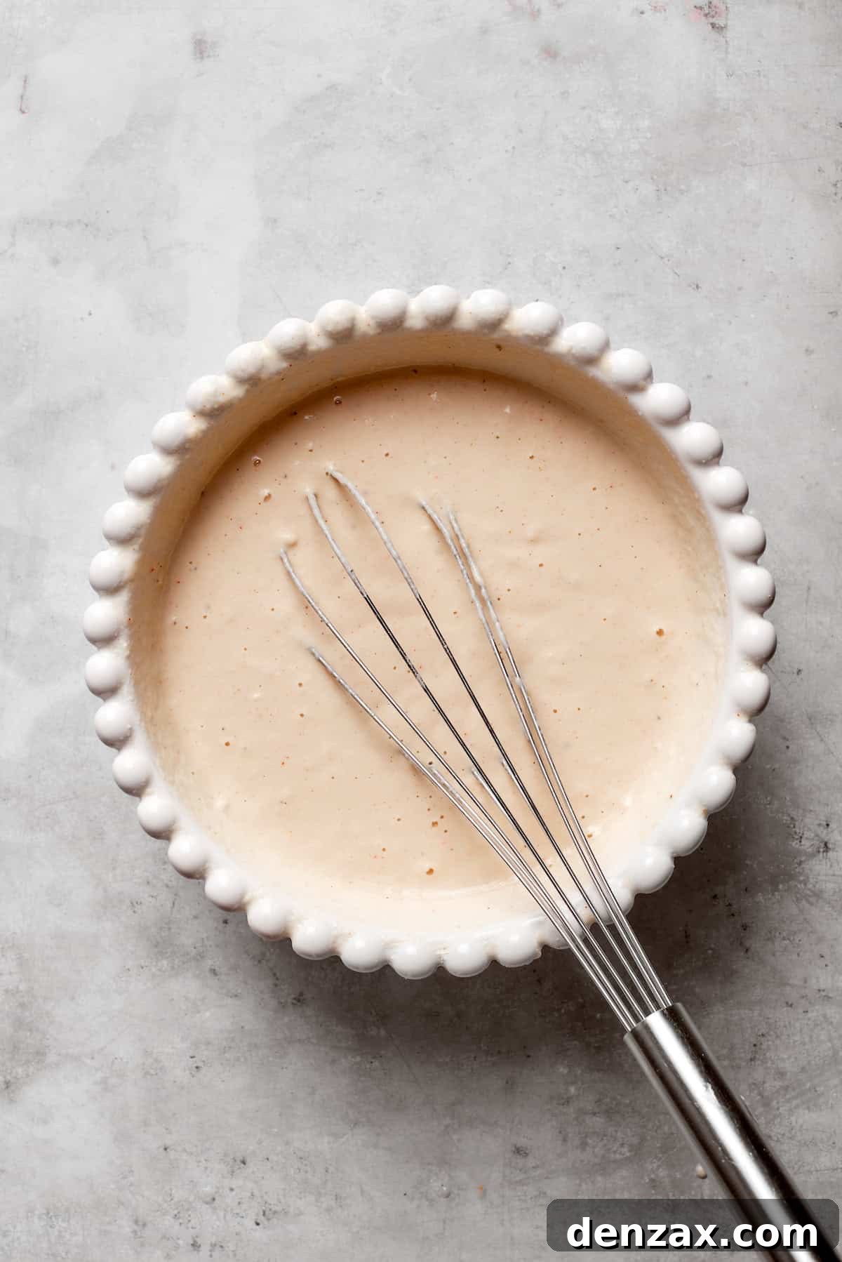 A whisk is mixing cold beer into the dry batter ingredients in a bowl.