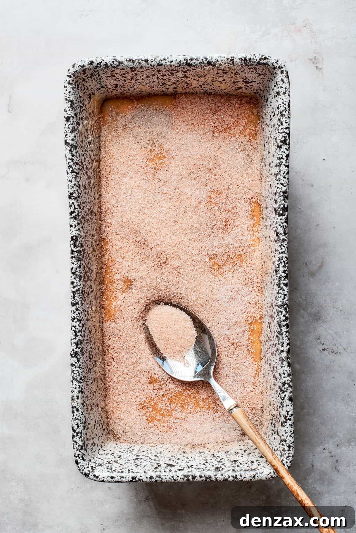 The cinnamon sugar topping is generously sprinkled over the surface of the bread batter in the loaf pan.