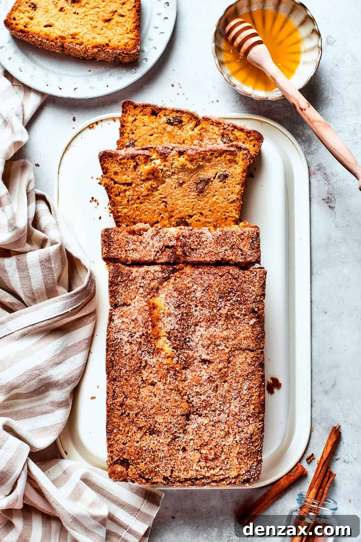 A serving platter holds a loaf of Amish friendship bread with one slice already cut, next to a small bowl of honey.