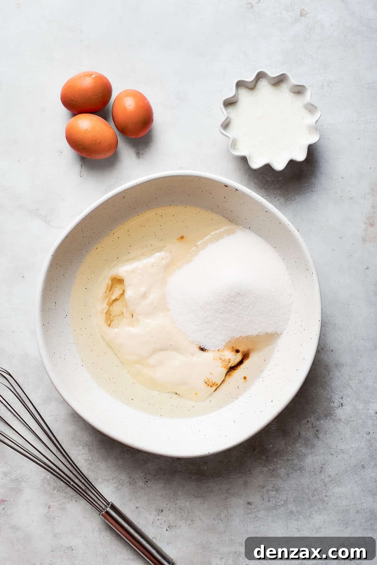 Granulated sugar is added to the wet batter of Amish friendship bread in a mixing bowl.