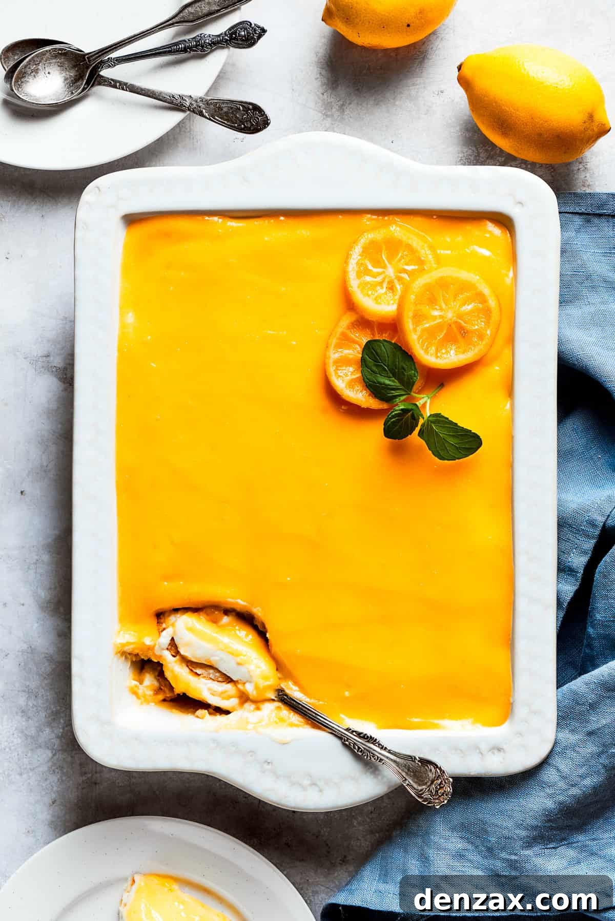A serving spoon is digging into the corner of a pan of lemon tiramisu, revealing its luscious layers.