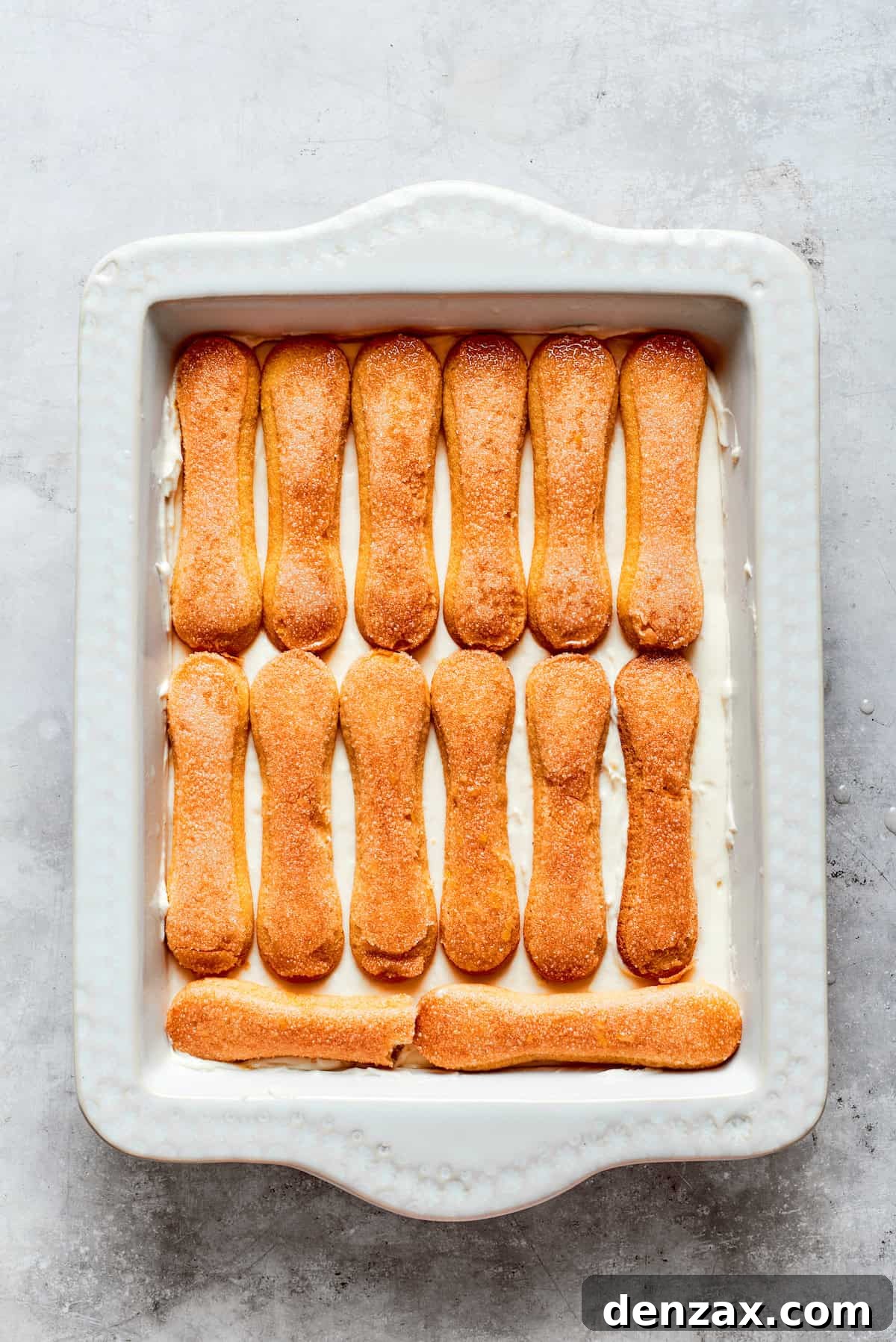 Another layer of lemon syrup-dipped ladyfinger cookies is carefully placed over the mascarpone cream, ready for more layers.