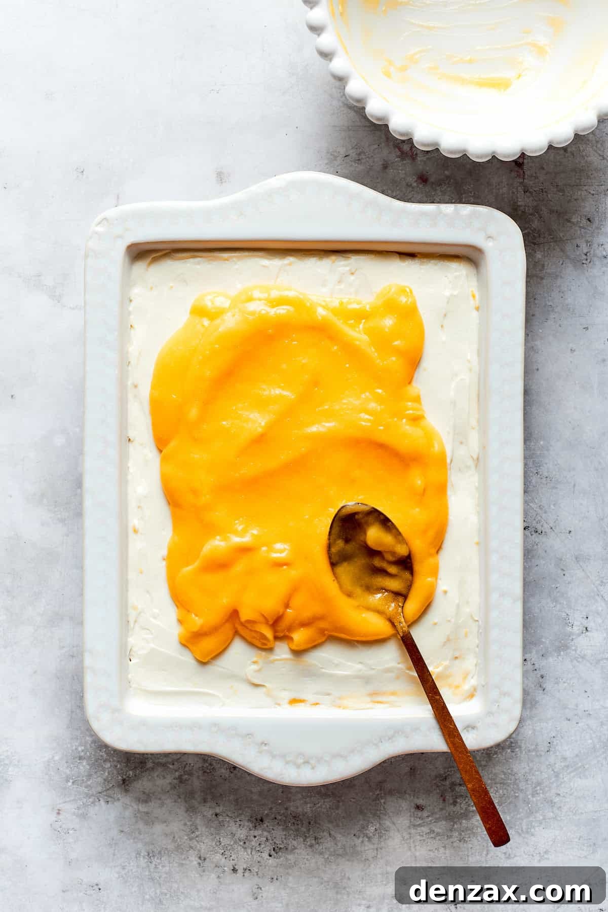 The final layer of smooth lemon curd is spread evenly over the assembled tiramisu, creating a vibrant topping.