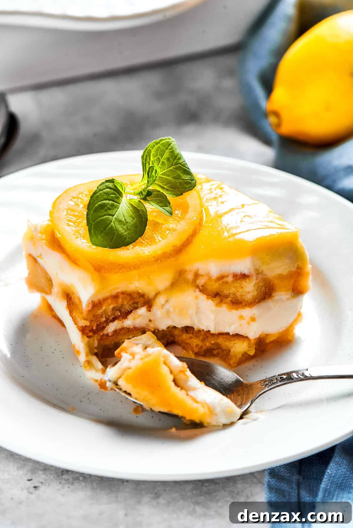 A fork is gently cutting into a serving of lemon tiramisu on a small white dessert plate, highlighting its soft layers and creamy texture.