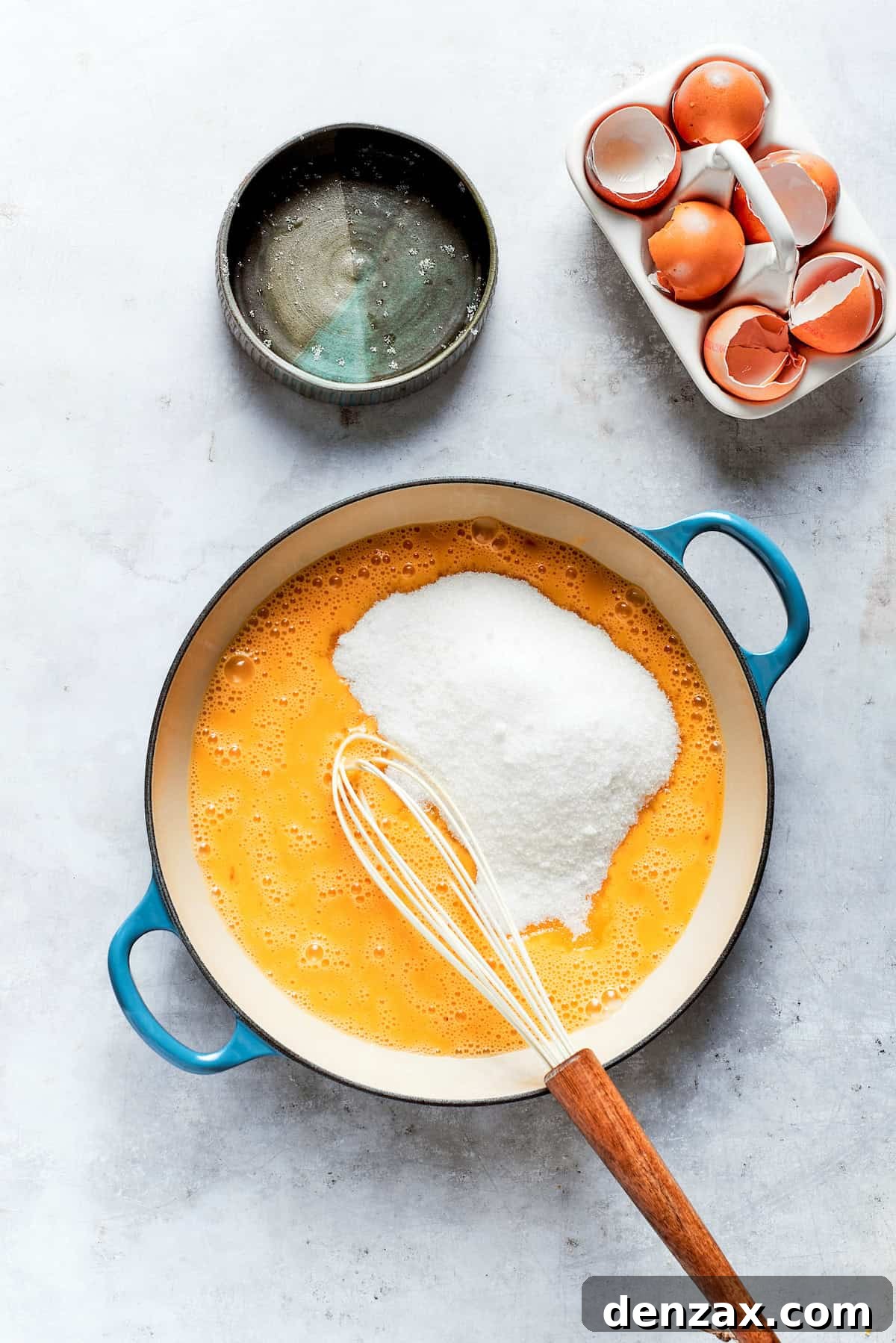 Granulated sugar is vigorously whisked into the lemon juice and eggs in a bowl, creating a smooth mixture for the curd.
