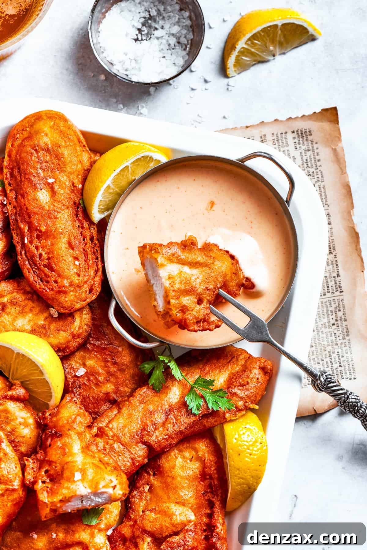 A golden-brown piece of crispy beer battered chicken being dipped into a spicy, creamy sauce. Other chicken pieces are artfully arranged nearby, showcasing the enticing texture of the fried coating.