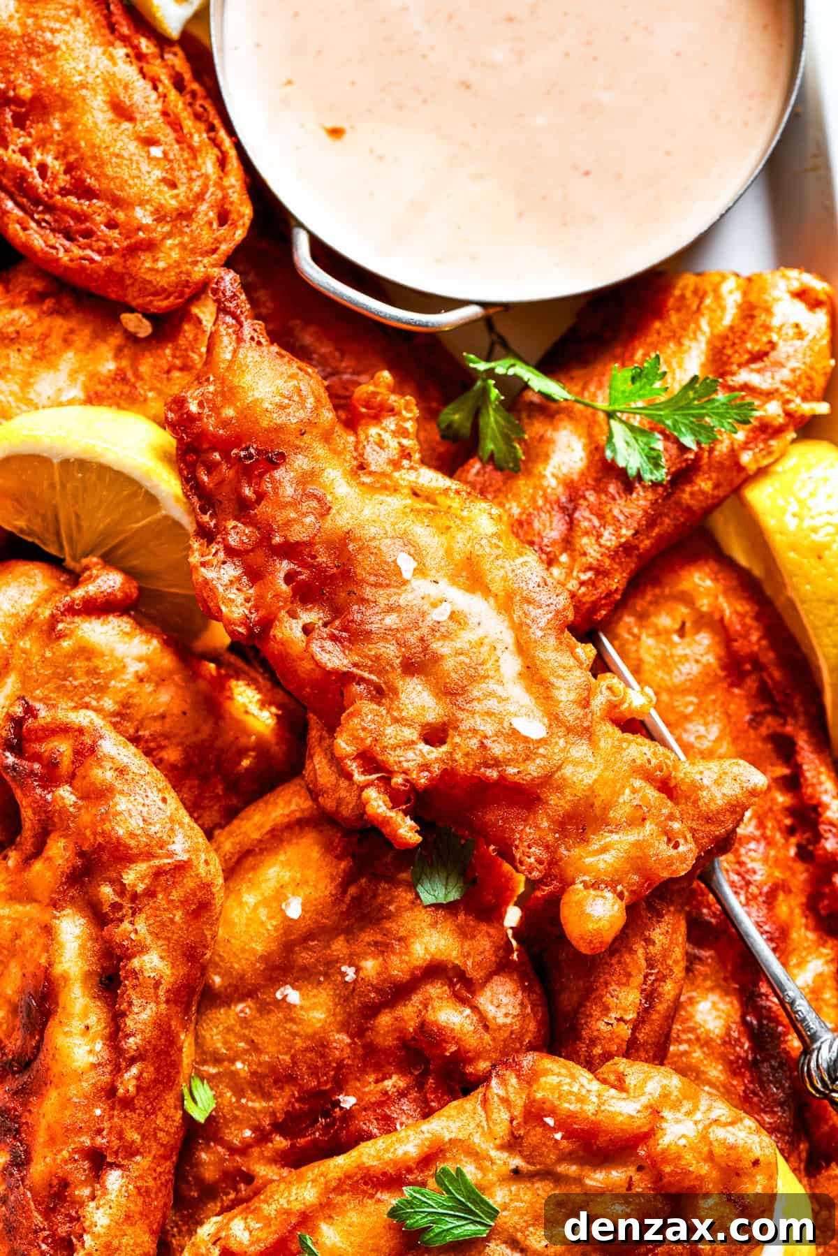 A close-up, mouth-watering shot of perfectly fried beer-battered chicken pieces arranged on a white plate, highlighting their golden, craggy, and incredibly crispy coating.