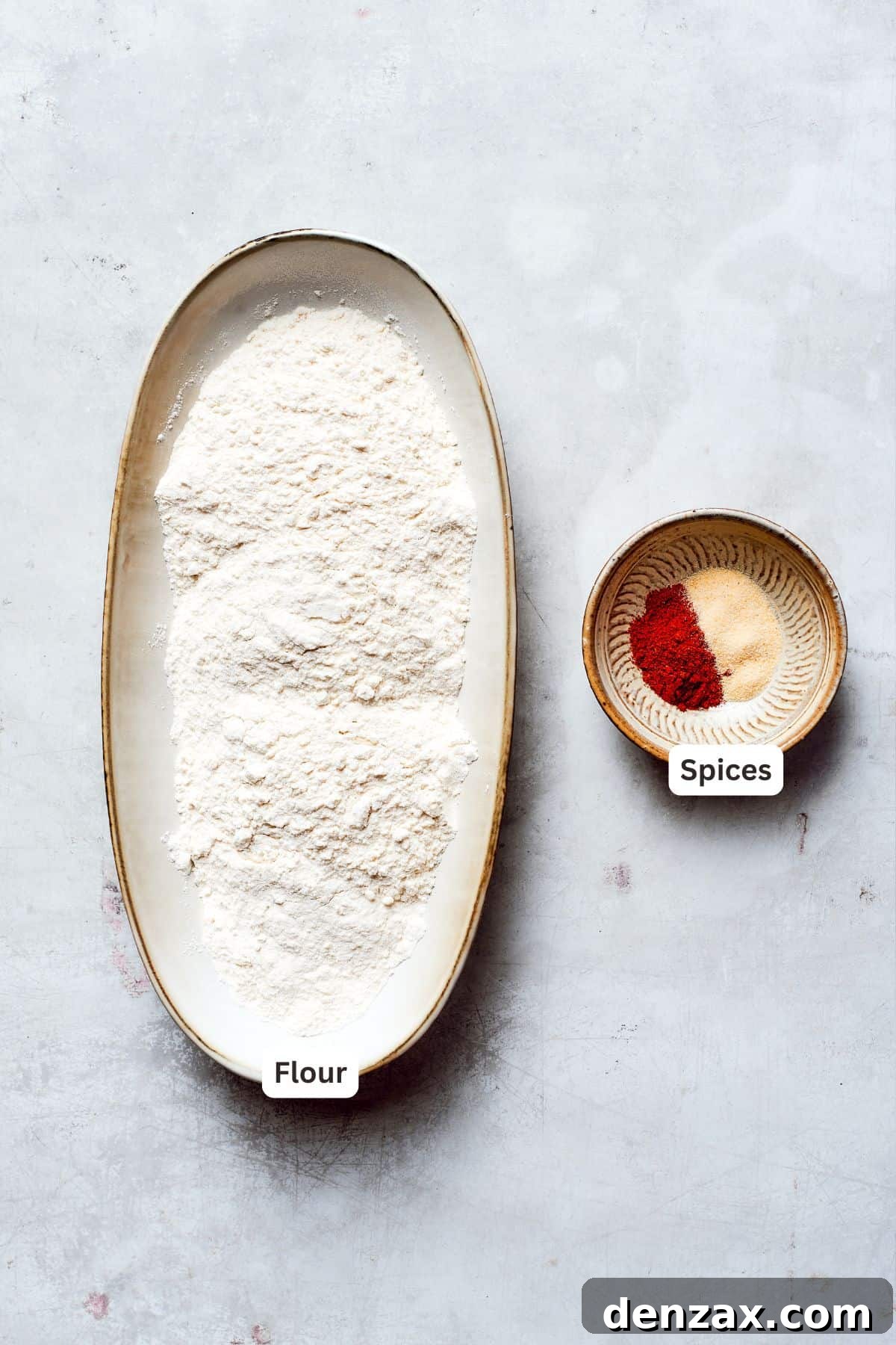 A trio of bowls showcasing labeled ingredients for the dredging mixture: all-purpose flour, a blend of flavorful spices, and seasoned chicken pieces ready for preparation.
