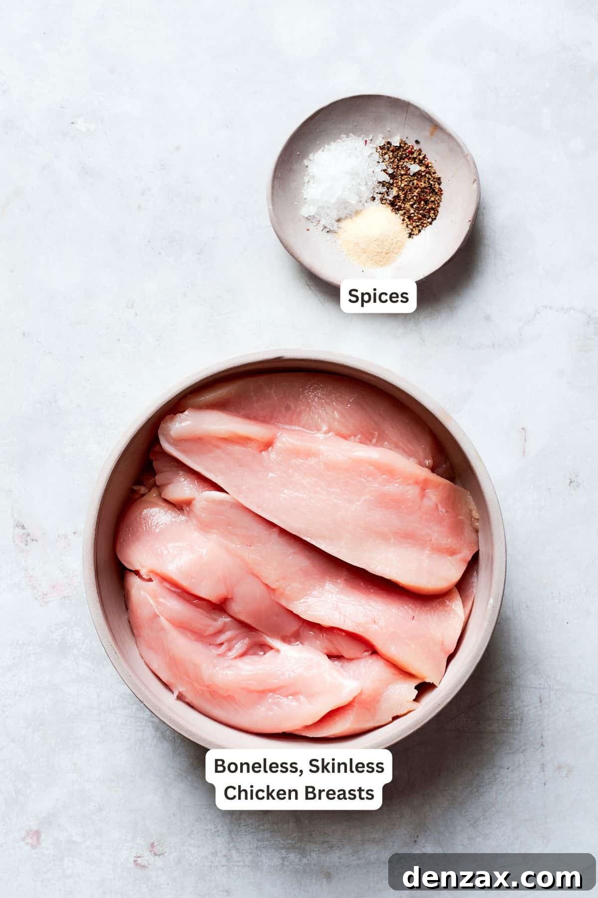 A clean, raw boneless, skinless chicken breast on a cutting board, alongside small bowls of seasonings including salt, pepper, and garlic powder, ready for preparation.
