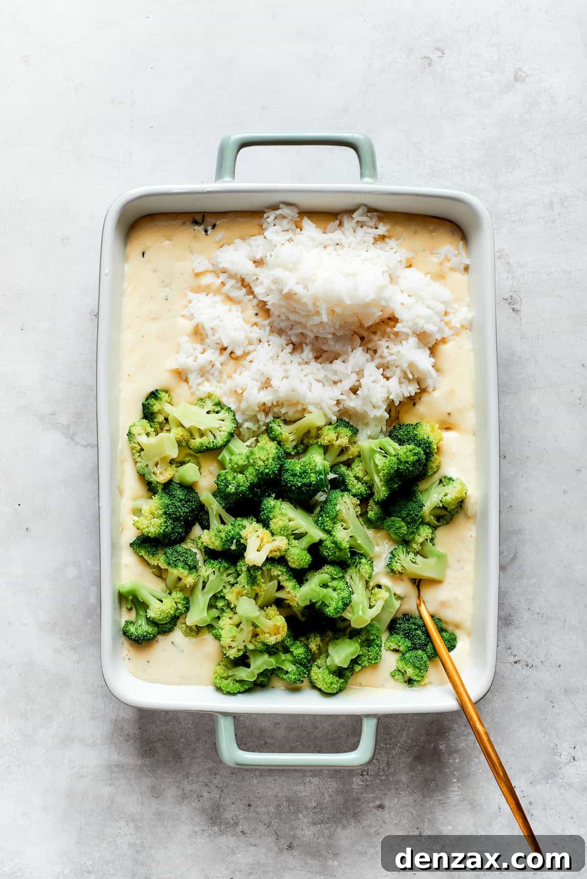 A baking pan with cheese sauce, broccoli, and rice.