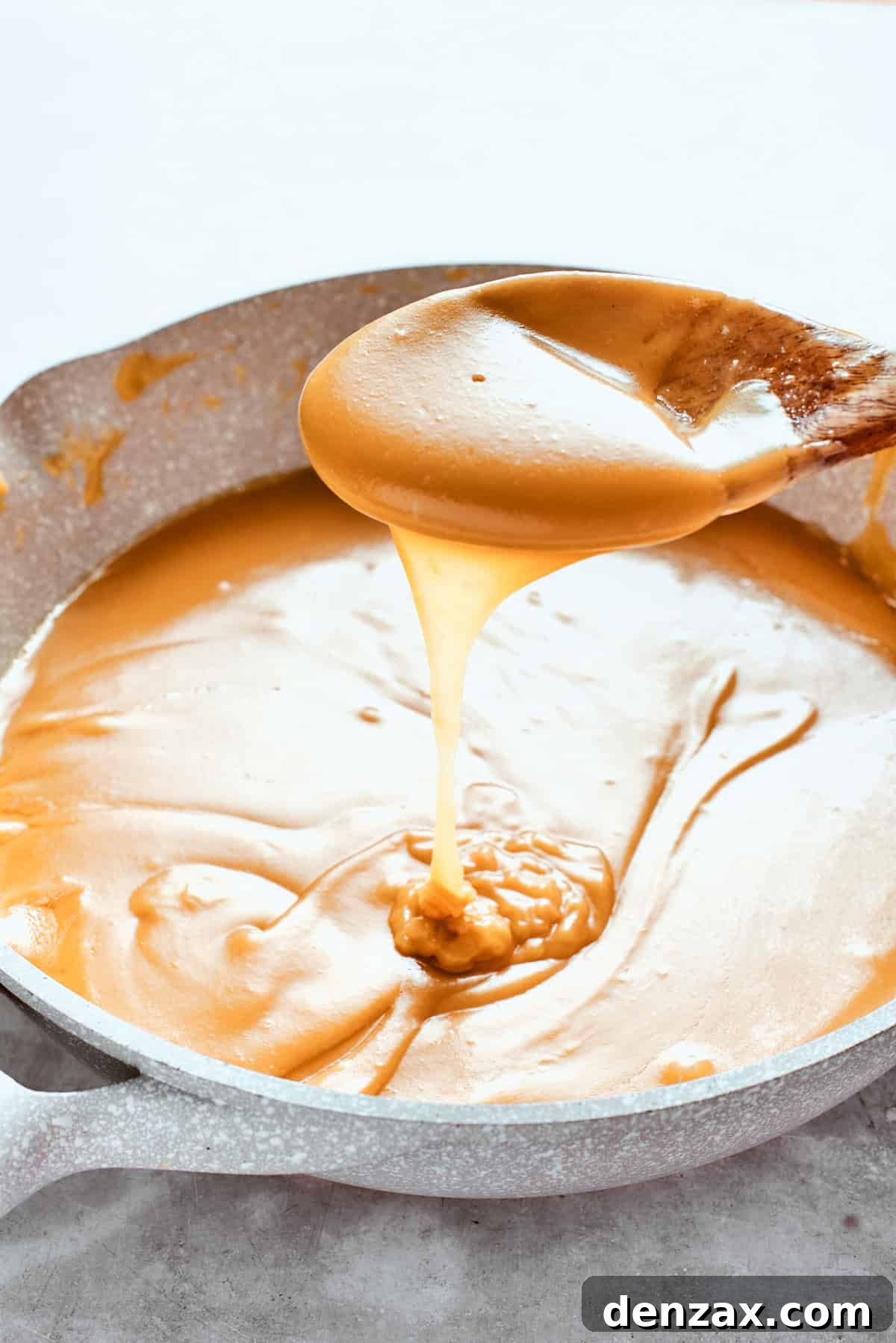 A spoon lifts up some caramel sauce, showing its thick, rich consistency.