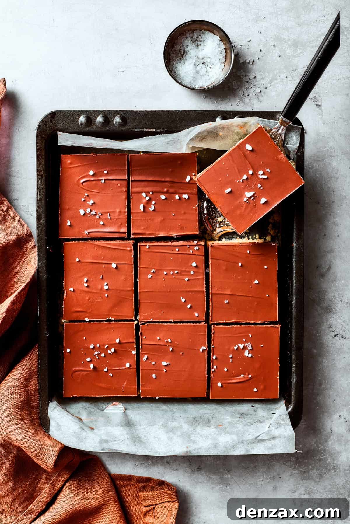 A serving utensil lifts out a perfectly cut square of millionaire bar from a pan.