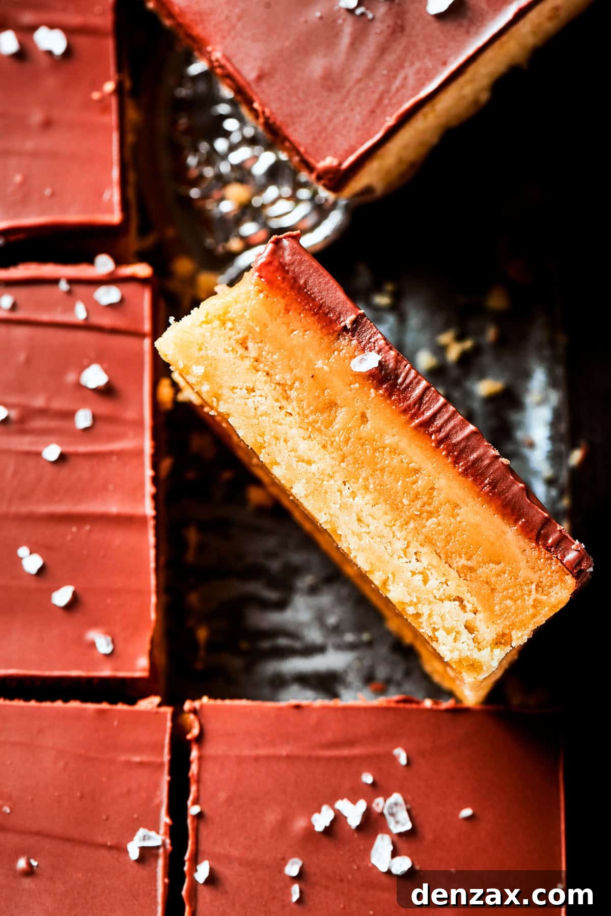 A single millionaire bar is turned on its side, resting atop a pan of freshly made millionaire bars, highlighting its beautiful layers.
