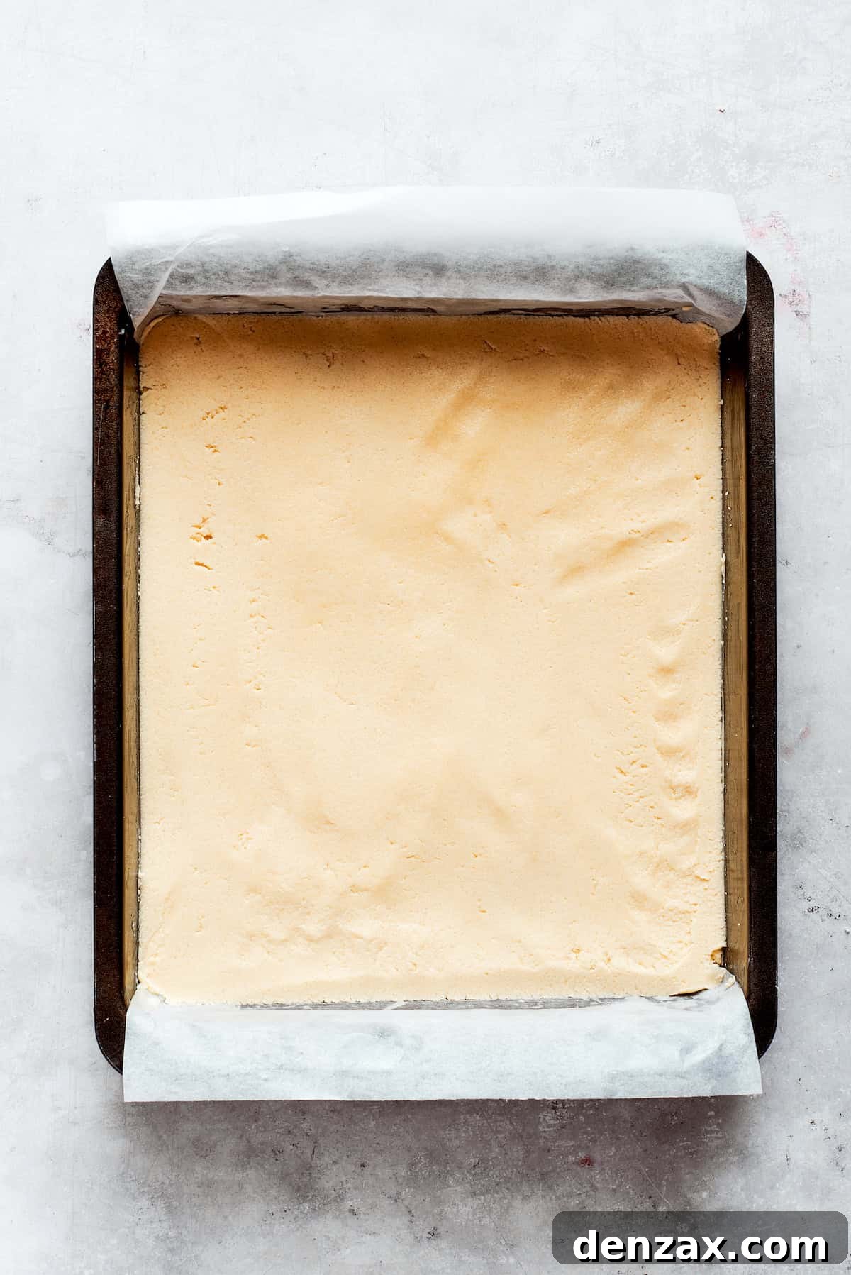 Shortbread dough is added to a parchment-lined baking pan, ready to be pressed evenly.