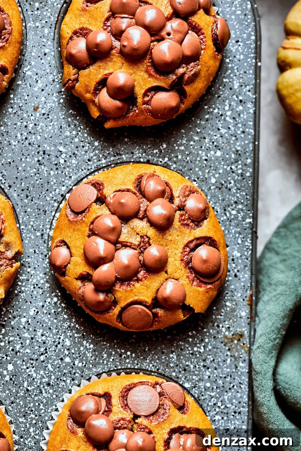 Three perfectly baked pumpkin chocolate chip muffins cooling in a muffin tin, showcasing their beautiful domed tops.