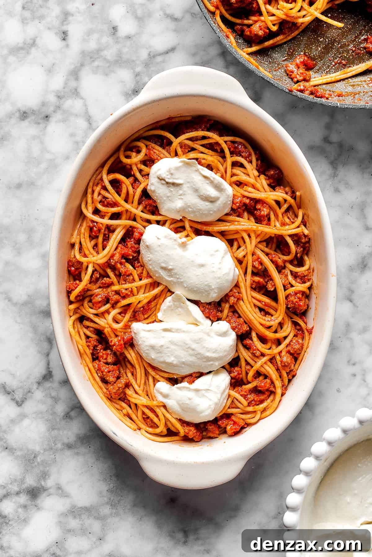 Spreading the creamy cheese mixture over a layer of spaghetti and meat sauce in a baking dish.