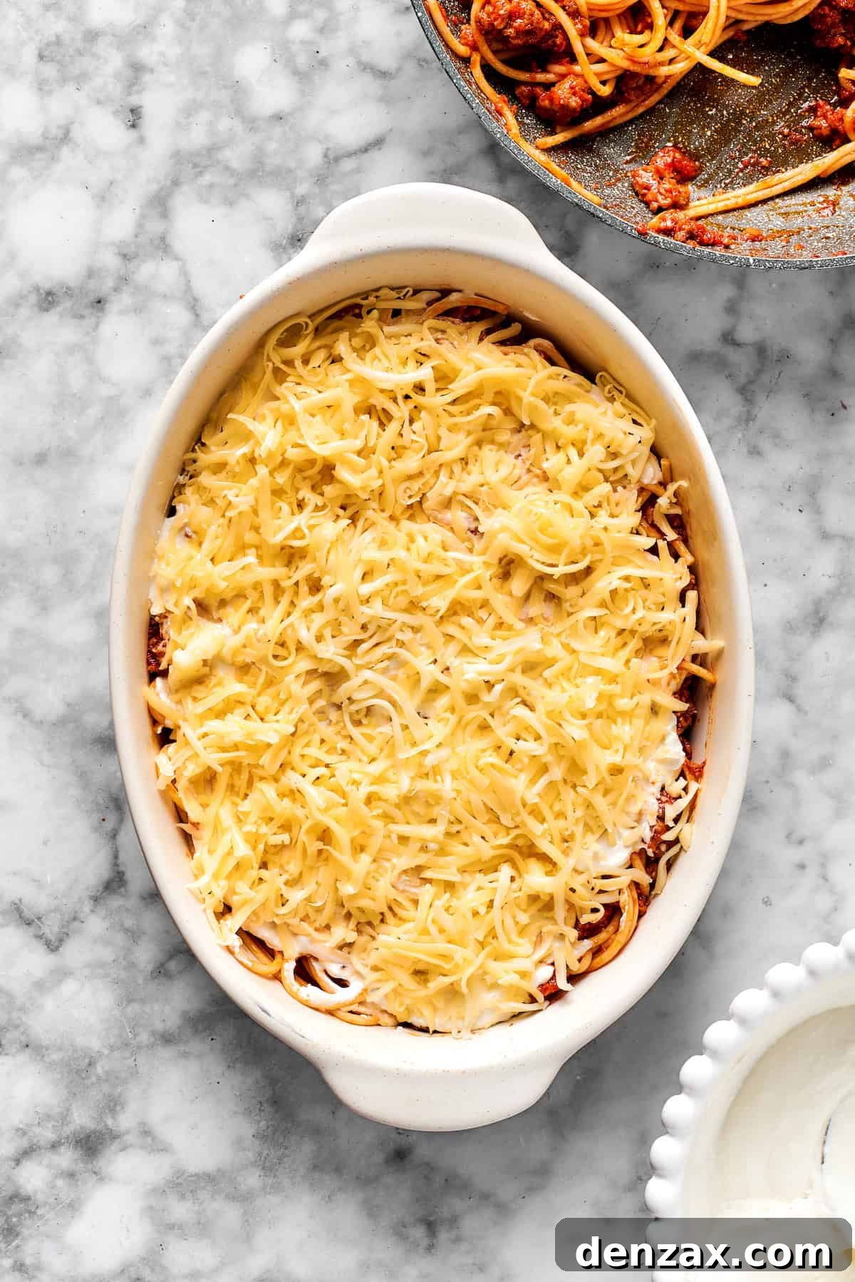 Adding a generous layer of shredded mozzarella cheese on top of spaghetti in a 9x13 dish before baking.